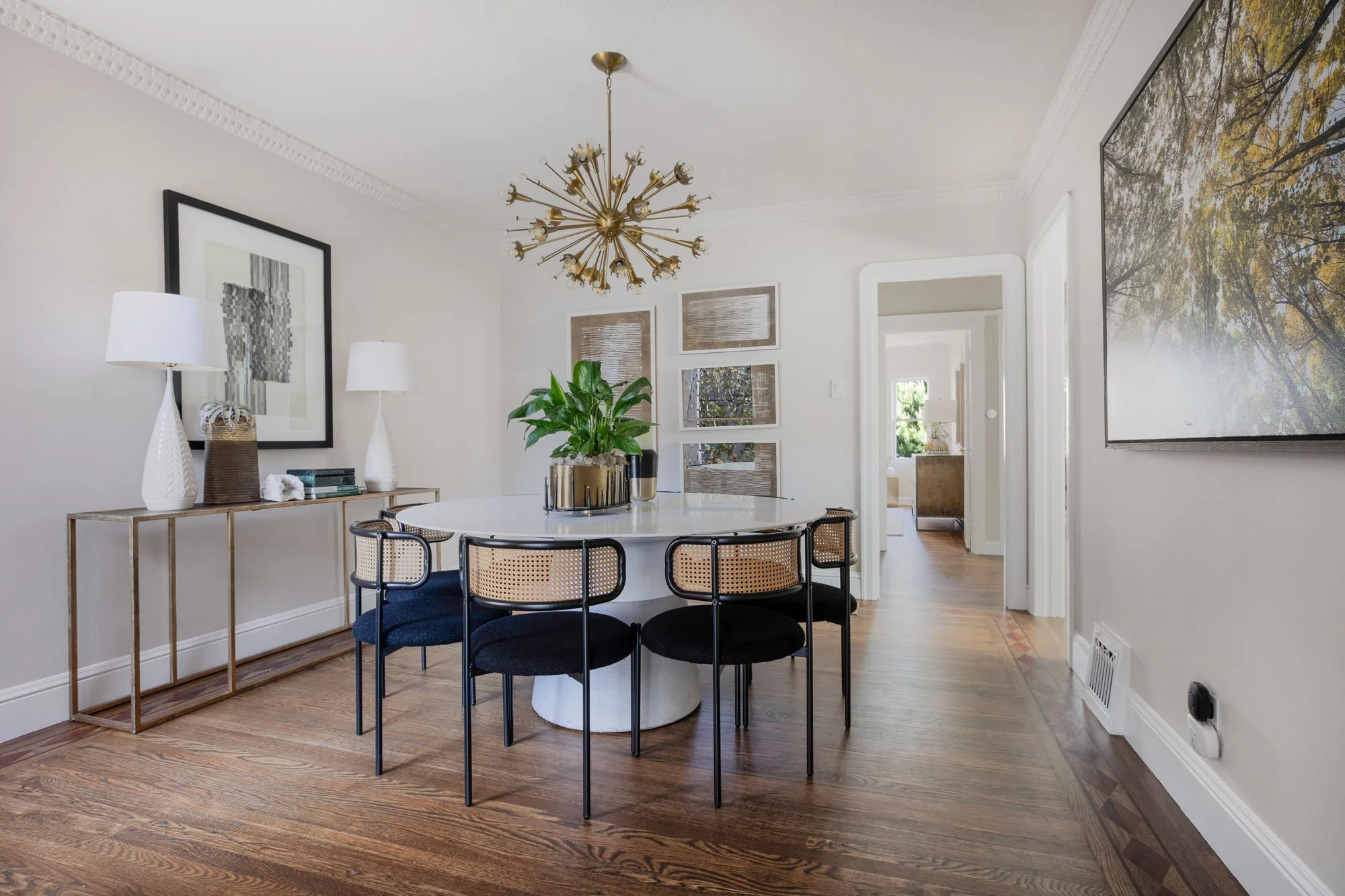 Formal dining room at 2872 25th St featuring a brass starburst chandelier, a white pedestal table with cane-back chairs, and original hardwood flooring.