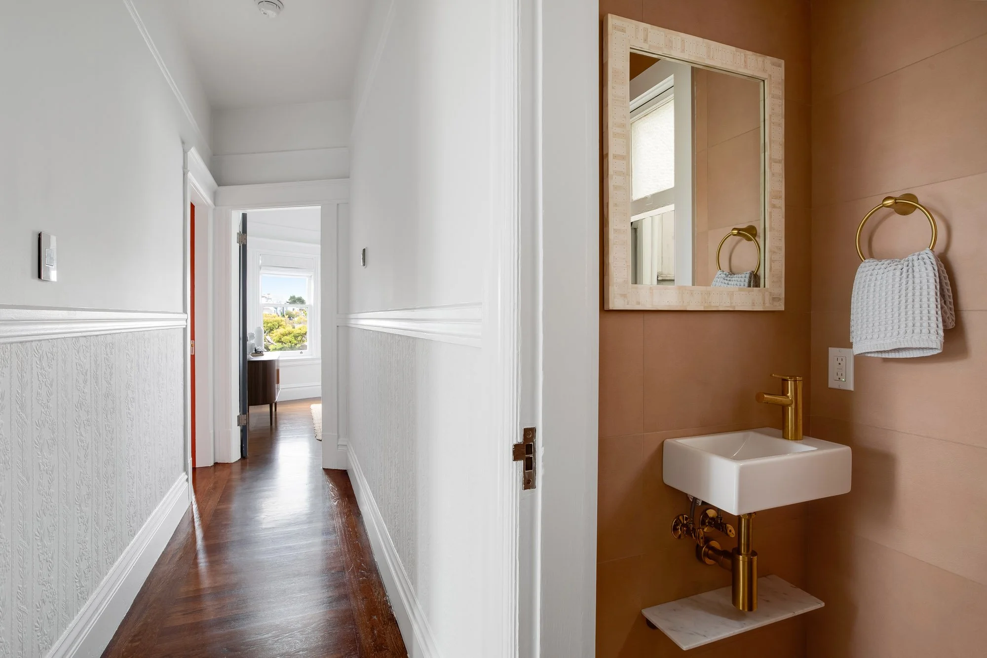 Victorian hallway with original stamped wall panels, hardwood floors, and crown molding alongside newly added powder room with terracotta tile, wall-mount sink, brass fixtures, and mosaic-framed mirror, Presidio Heights, San Francisco