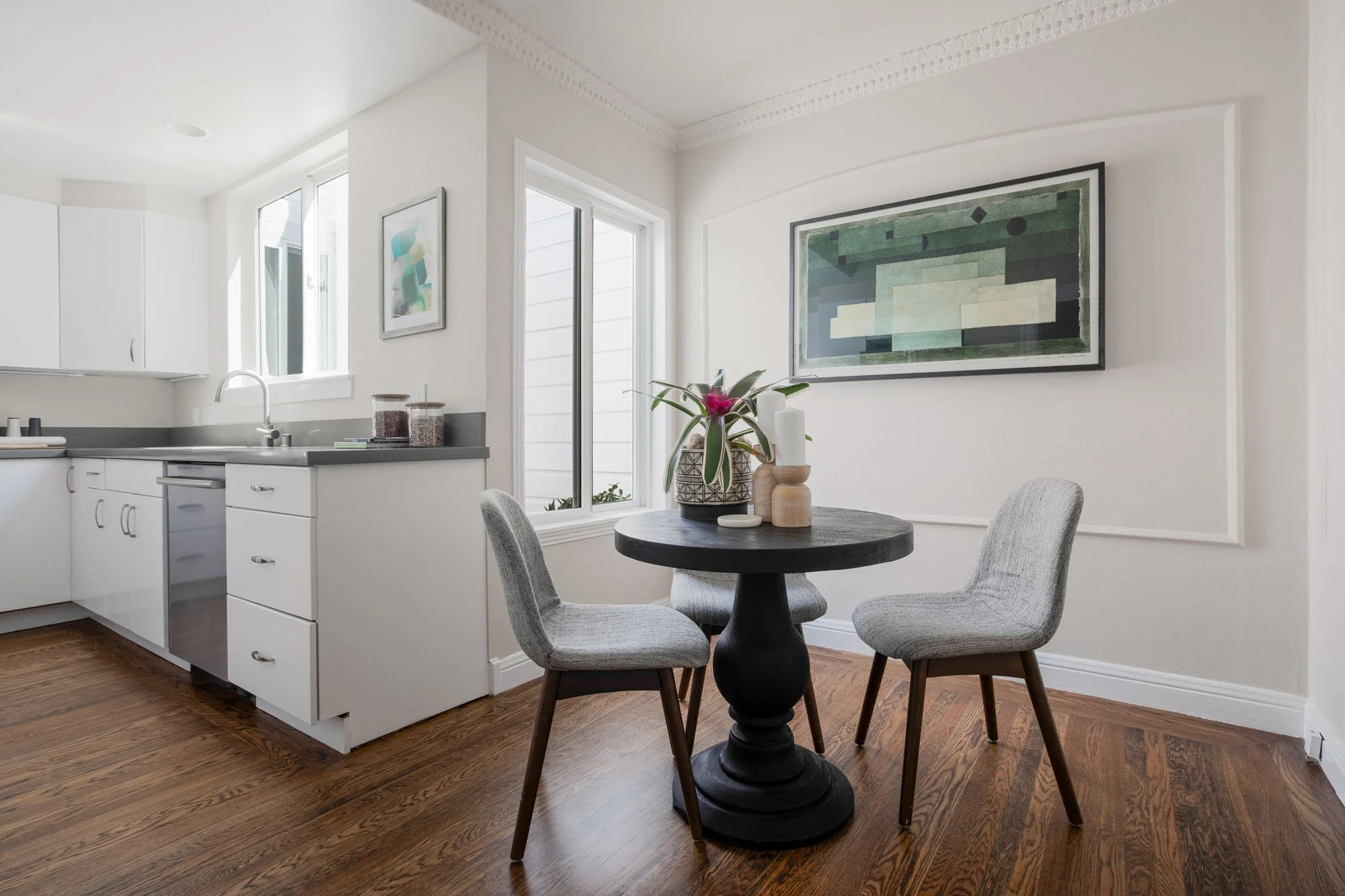 Bright breakfast nook adjacent to the kitchen with a round black pedestal table, modern grey upholstered chairs, and decorative wall molding.