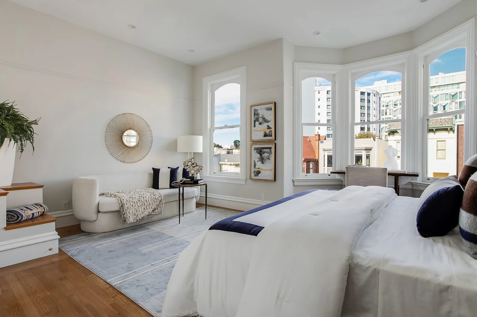 ModModern primary suite sitting area with a contemporary white sofa, chic gold mirror, and views of the historic San Francisco neighborhood through large windows.