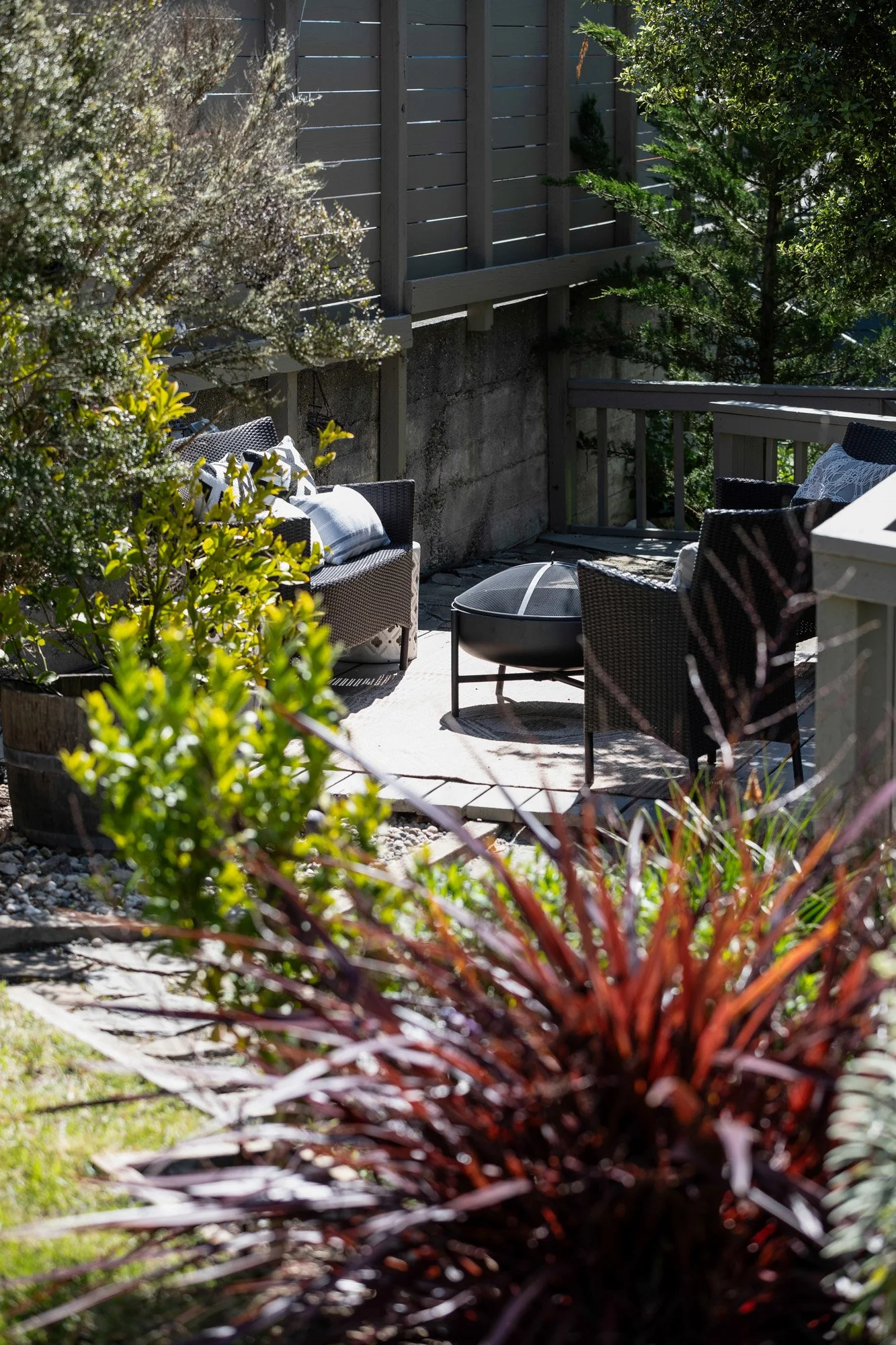 Close-up of a cozy backyard seating area with a black fire pit, surrounded by professional landscaping and ornamental grasses.