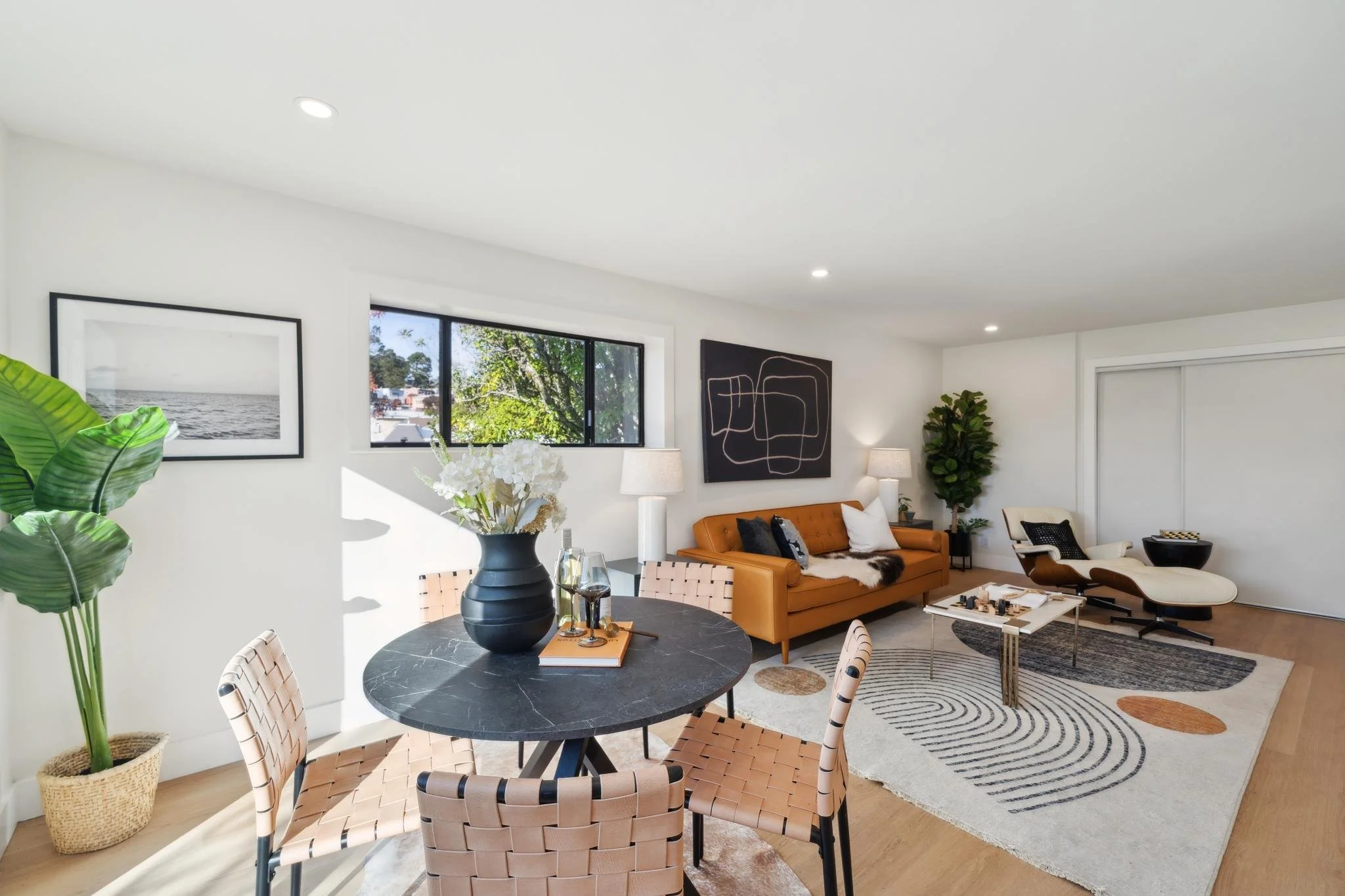 Bright lower-level sitting room with a black marble dining table, woven leather chairs, and large windows overlooking the lush San Francisco landscape.