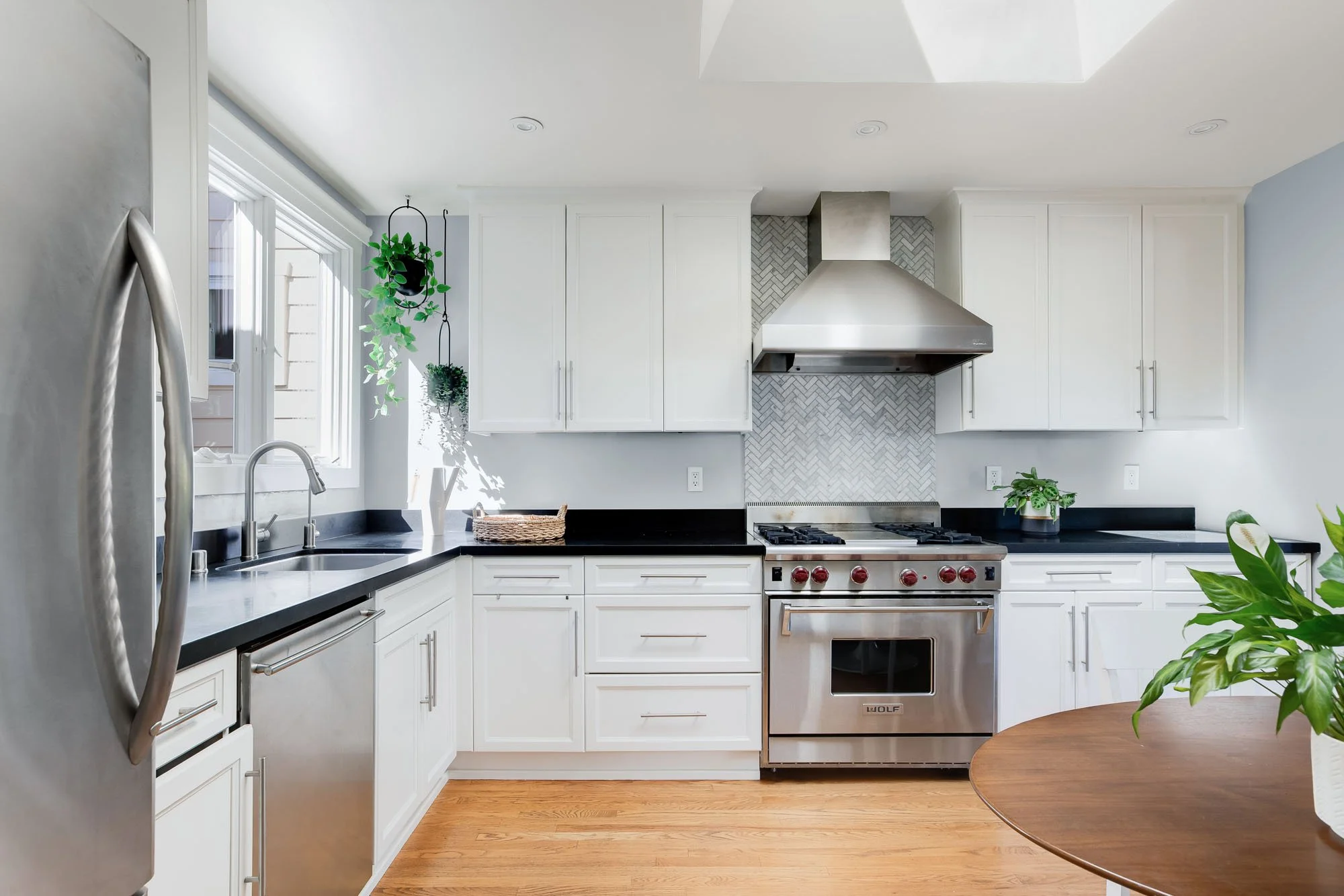 Symmetrical view of the kitchen’s main cooking area with white shaker cabinets, a large stainless steel vent hood, and a deep undermount sink.