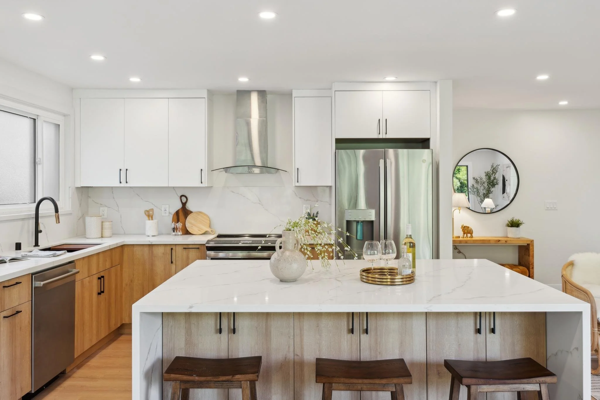 Luxury kitchen with dual-tone cabinetry, white marble backsplash, stainless steel appliances, and a large waterfall edge island with dark wood bar stools.