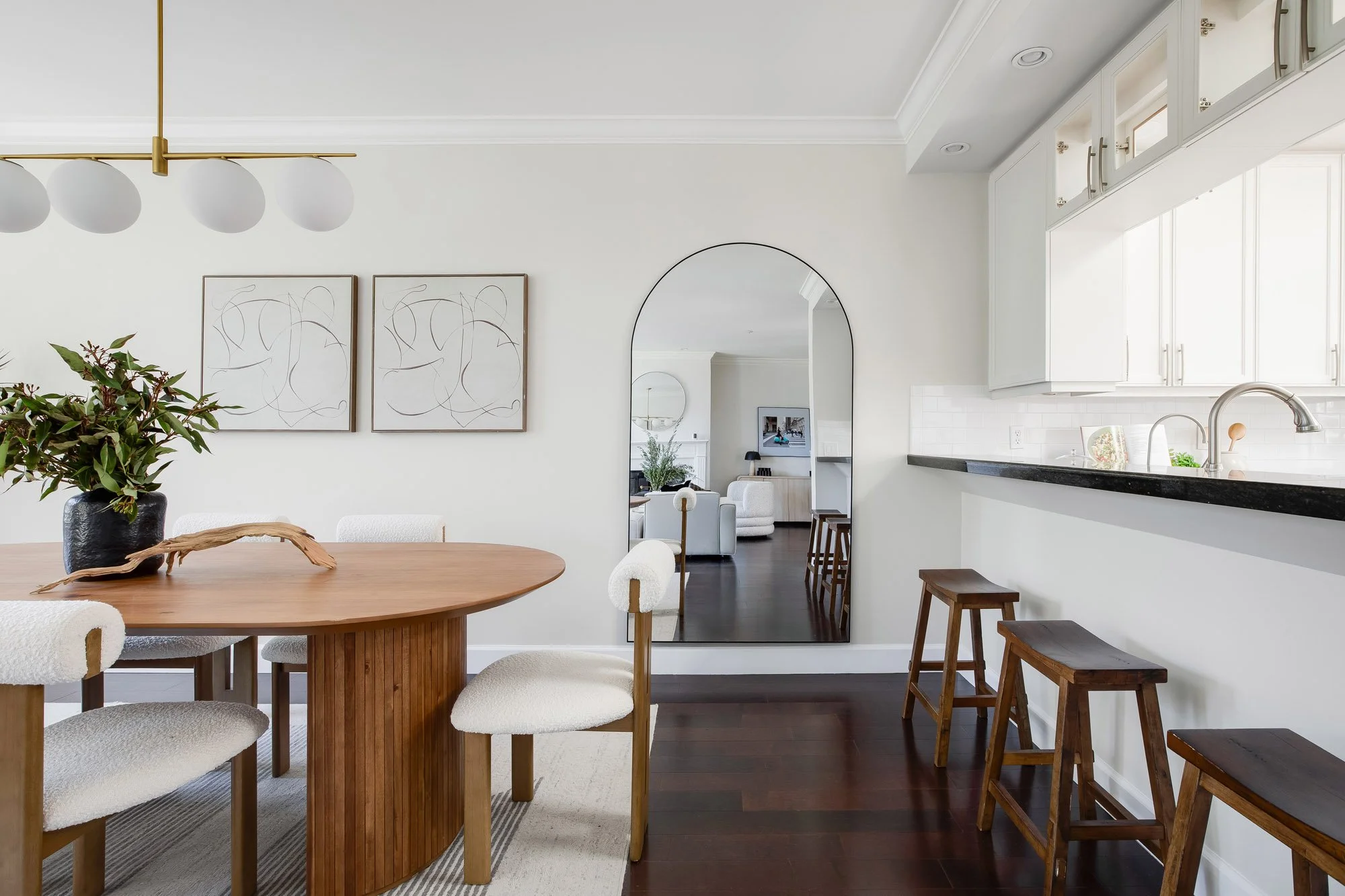 Dining area and kitchen pass-through at 2172 Fell Street San Francisco with oval walnut dining table, arched full-length mirror, brass pendant light, and white upper cabinets with dark granite counter
