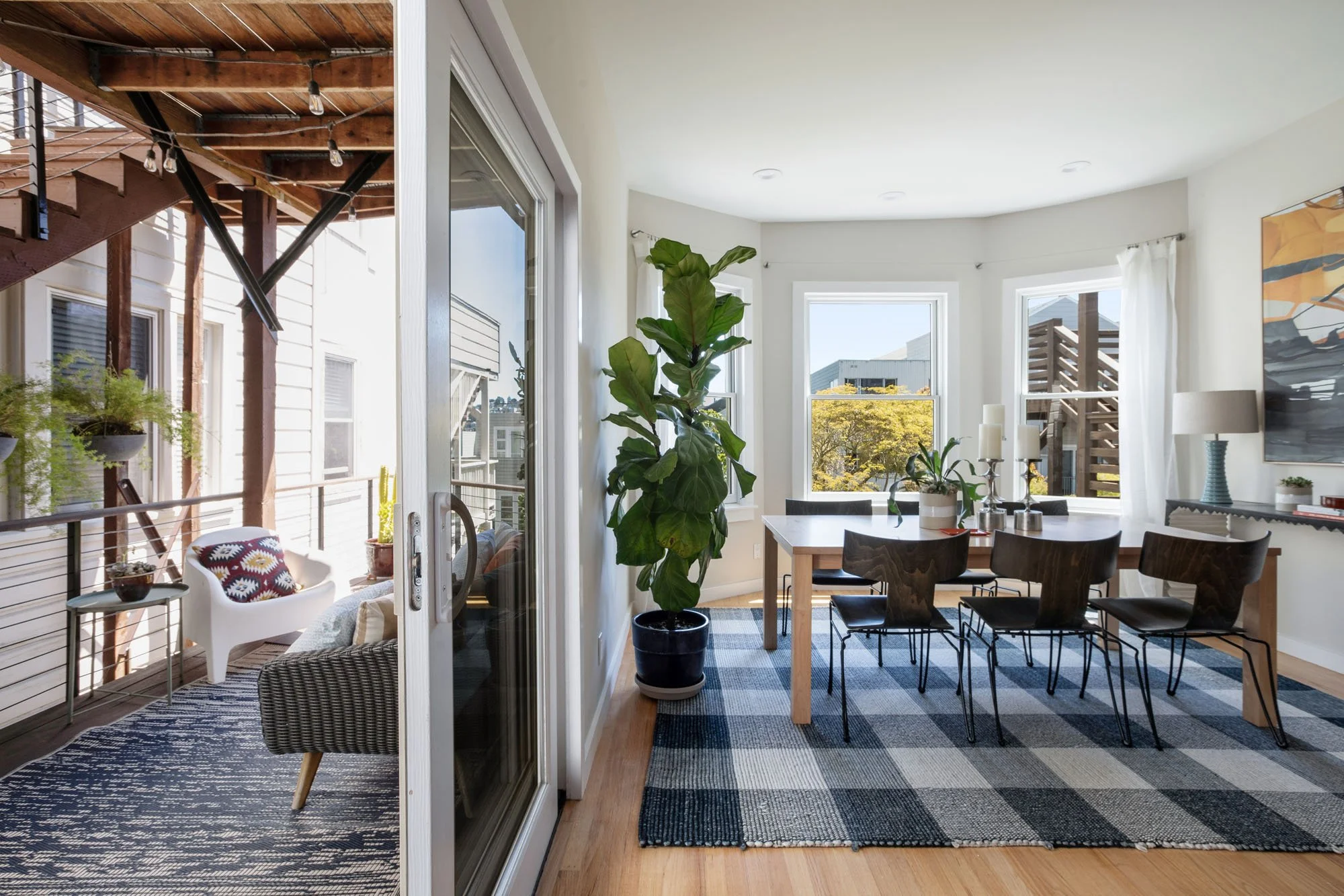 Bright dining area showing the transition through sliding doors to a private outdoor deck with seating and city views.