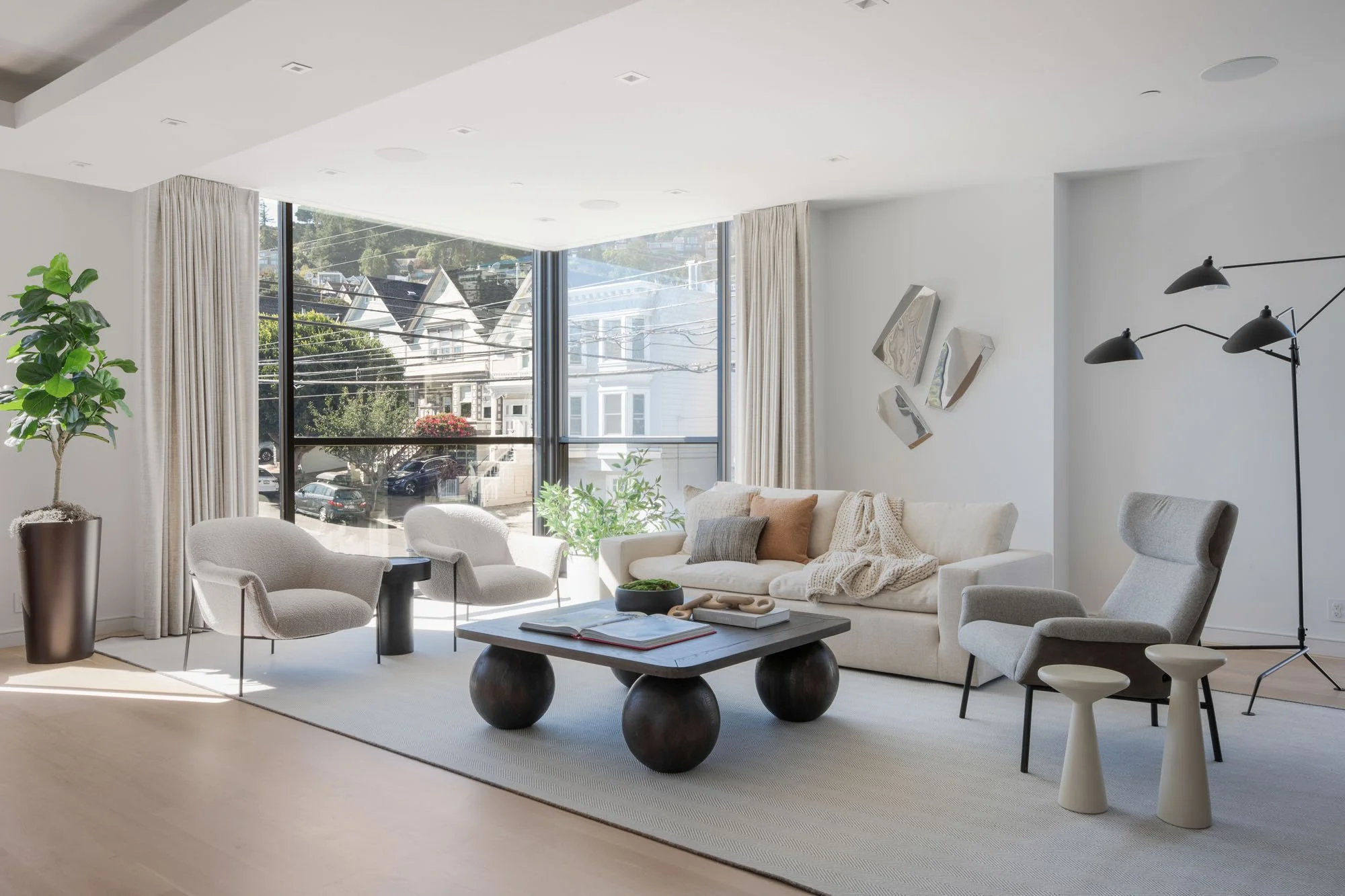 Luxury living room with large corner windows overlooking San Francisco Victorian houses. Features modern boucle chairs, a unique sphere-leg coffee table, and an airy, minimalist design.