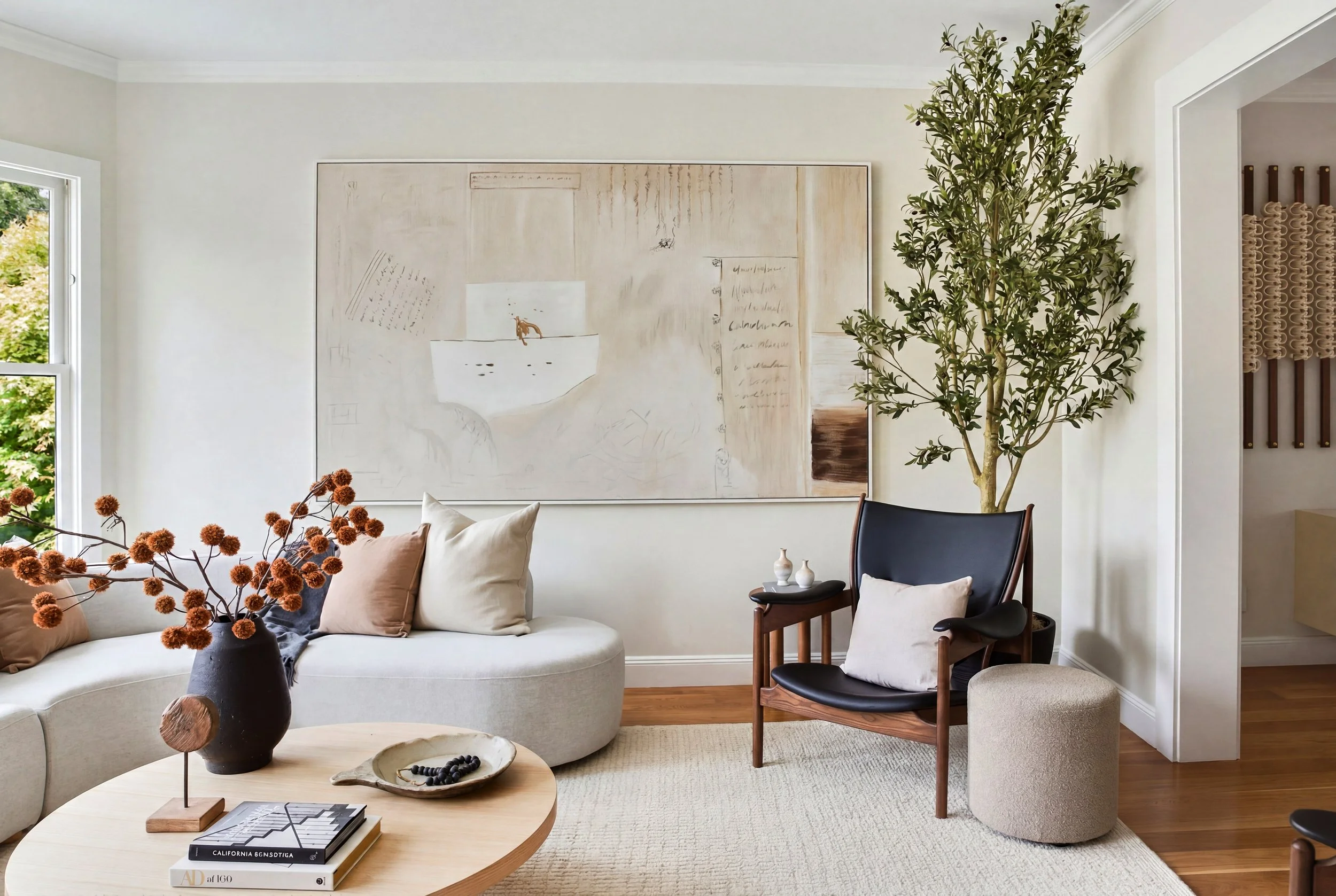 Living room with curved white sectional sofa, walnut lounge chair, round wood coffee table, and potted olive tree, at 771 Elizabeth Street