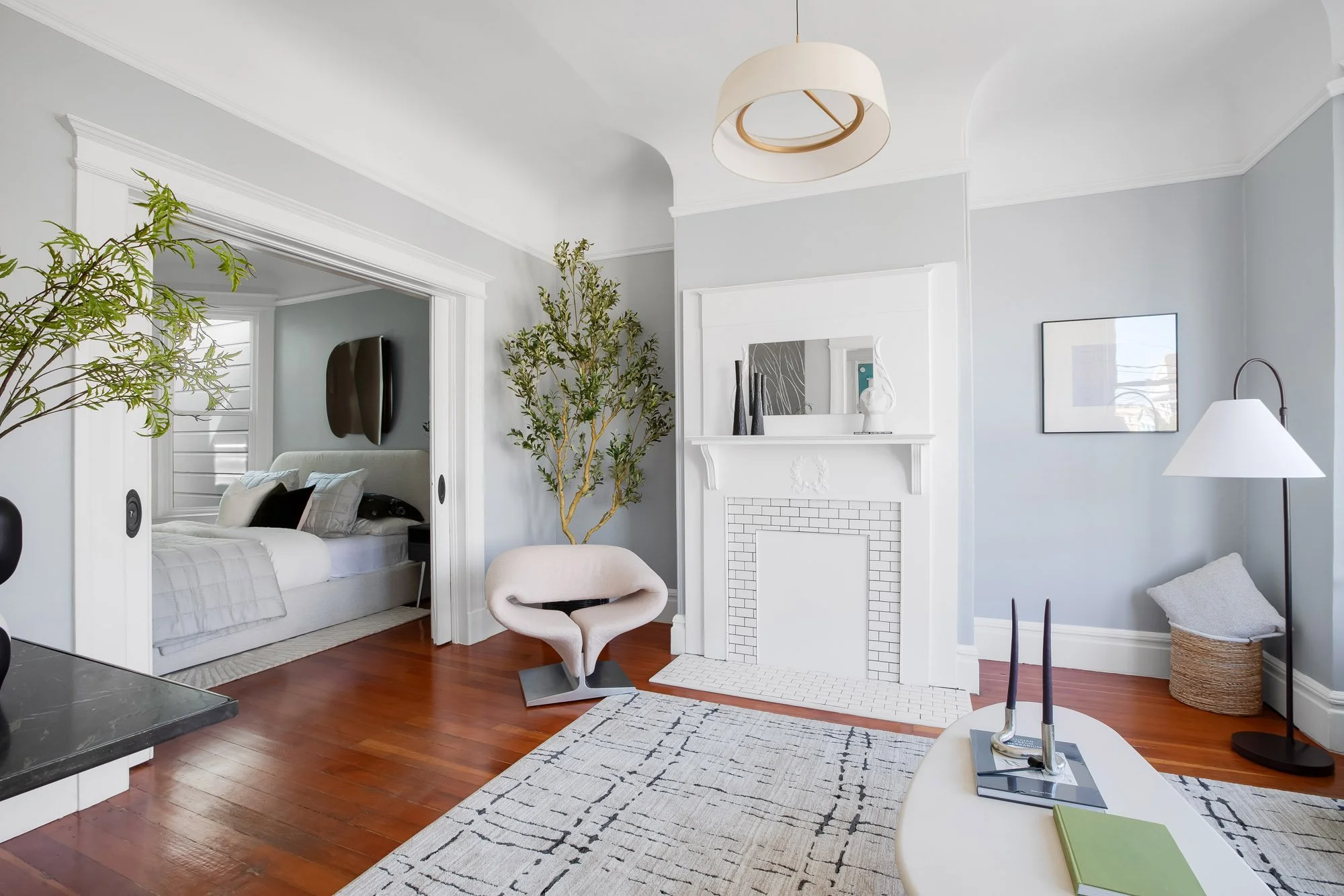 Living room opening through pocket doors to a bedroom, with fireplace mantel and bay window seating area