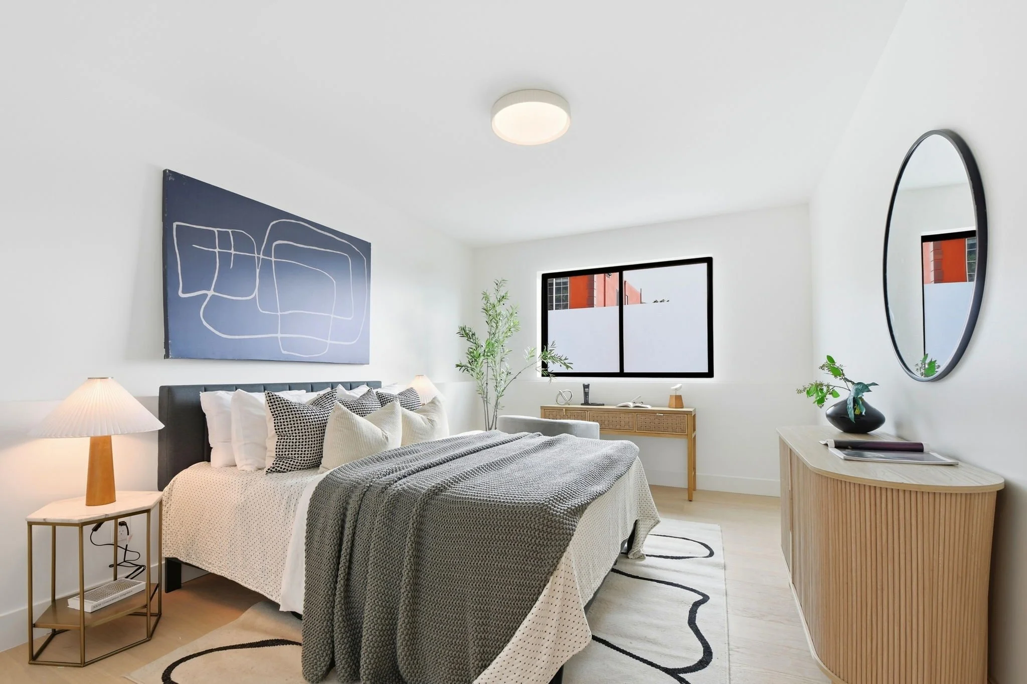 Sophisticated bedroom suite with blue abstract wall art, a fluted wood console, and a large round mirror reflecting a bright, modern interior.