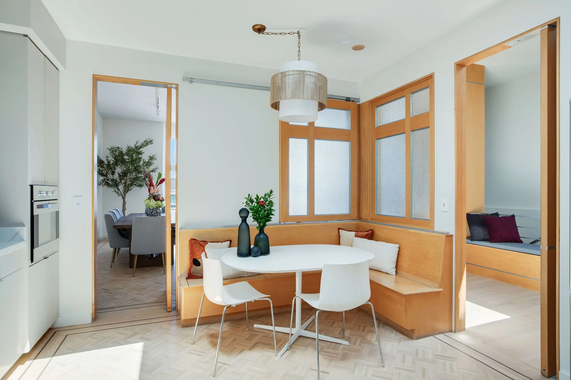 Stylish dining nook with a round white table and integrated wood banquette seating, highlighting the architectural flow between the kitchen and the formal dining room.