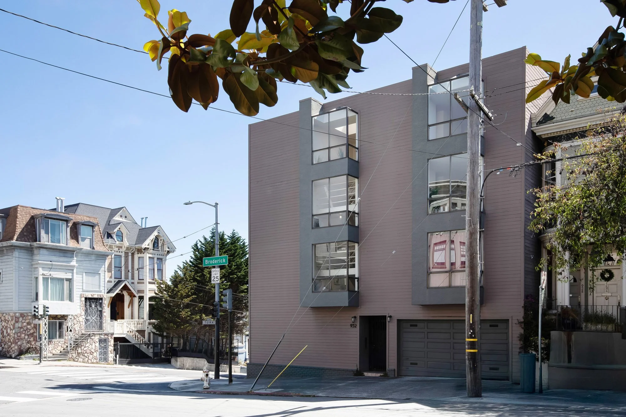 Corner exterior of 932 Broderick Street showing the gray modern facade alongside neighboring Victorian houses in San Francisco.