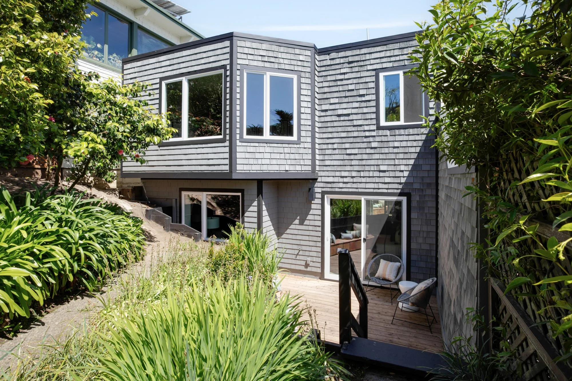 Architectural view of a multi-level San Francisco hillside residence with tiered garden landscaping, grey wood shingle exterior, and multiple private outdoor living spaces.