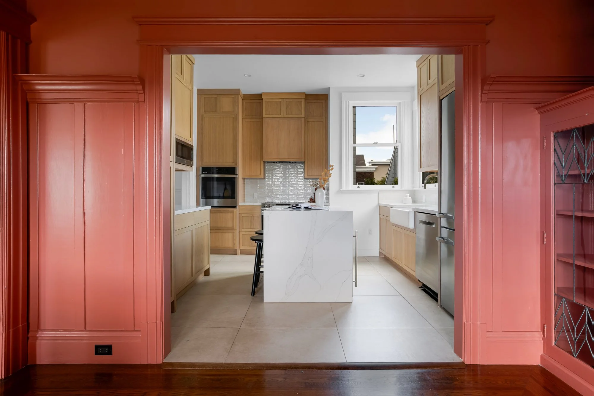 View from color-drenched formal dining room into renovated chef's kitchen through original Victorian molded doorframe with leaded-glass built-in cabinetry, Presidio Heights flat, San Francisco