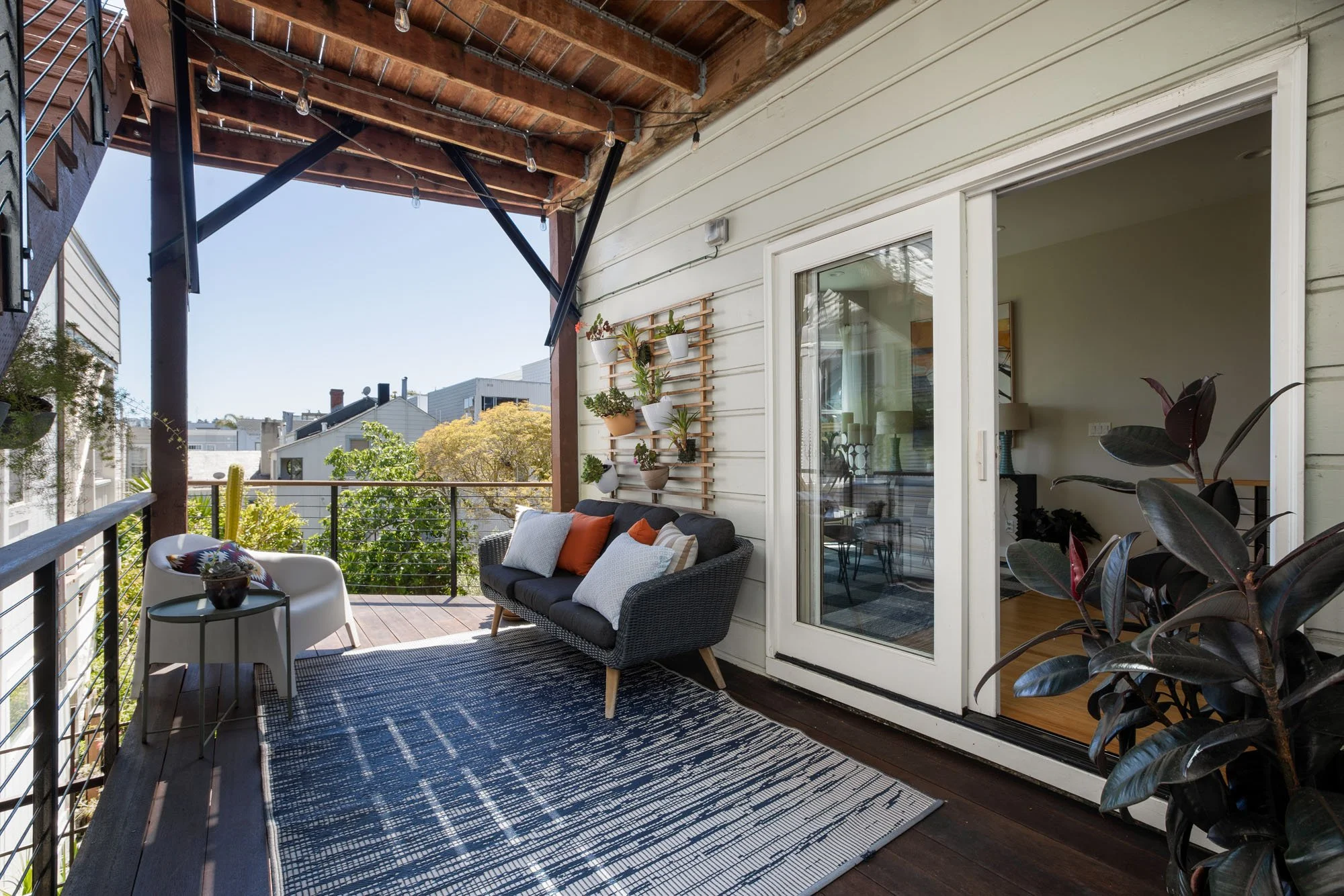 Private deeded outdoor living space with a sofa and string lights, featuring sliding glass doors that lead into a bright, modern interior.