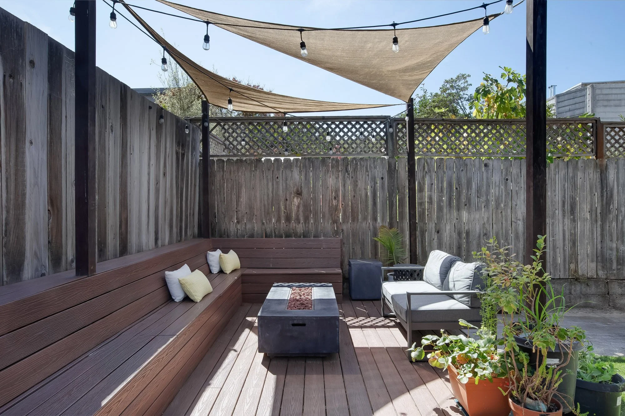 Rear yard lounge area with a fire table, built-in bench seating, and sail-shade canopy