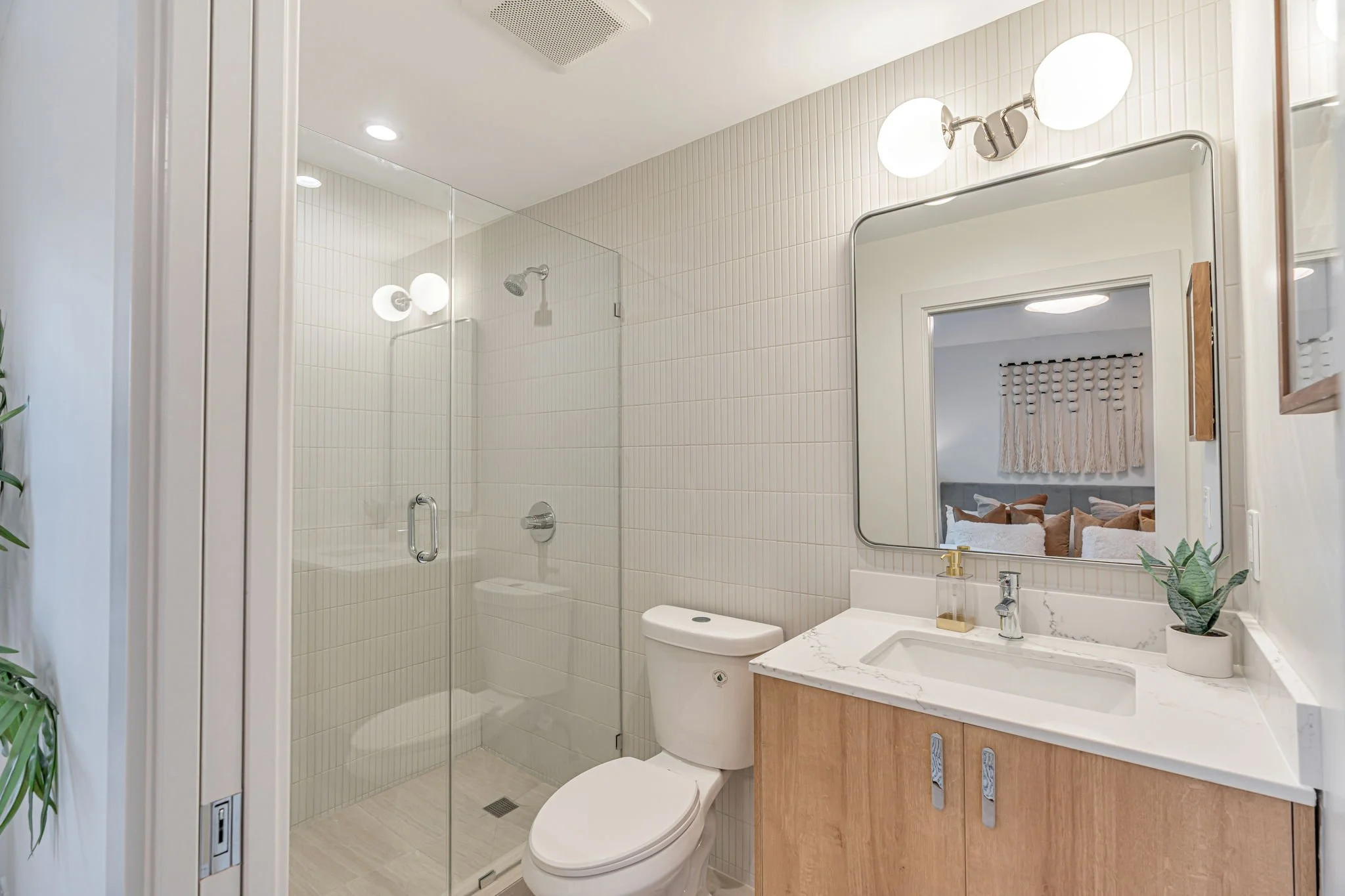 Contemporary ensuite bathroom featuring a frameless glass walk-in shower with vertical white tile, a light wood floating vanity, and a minimalist rectangular mirror.