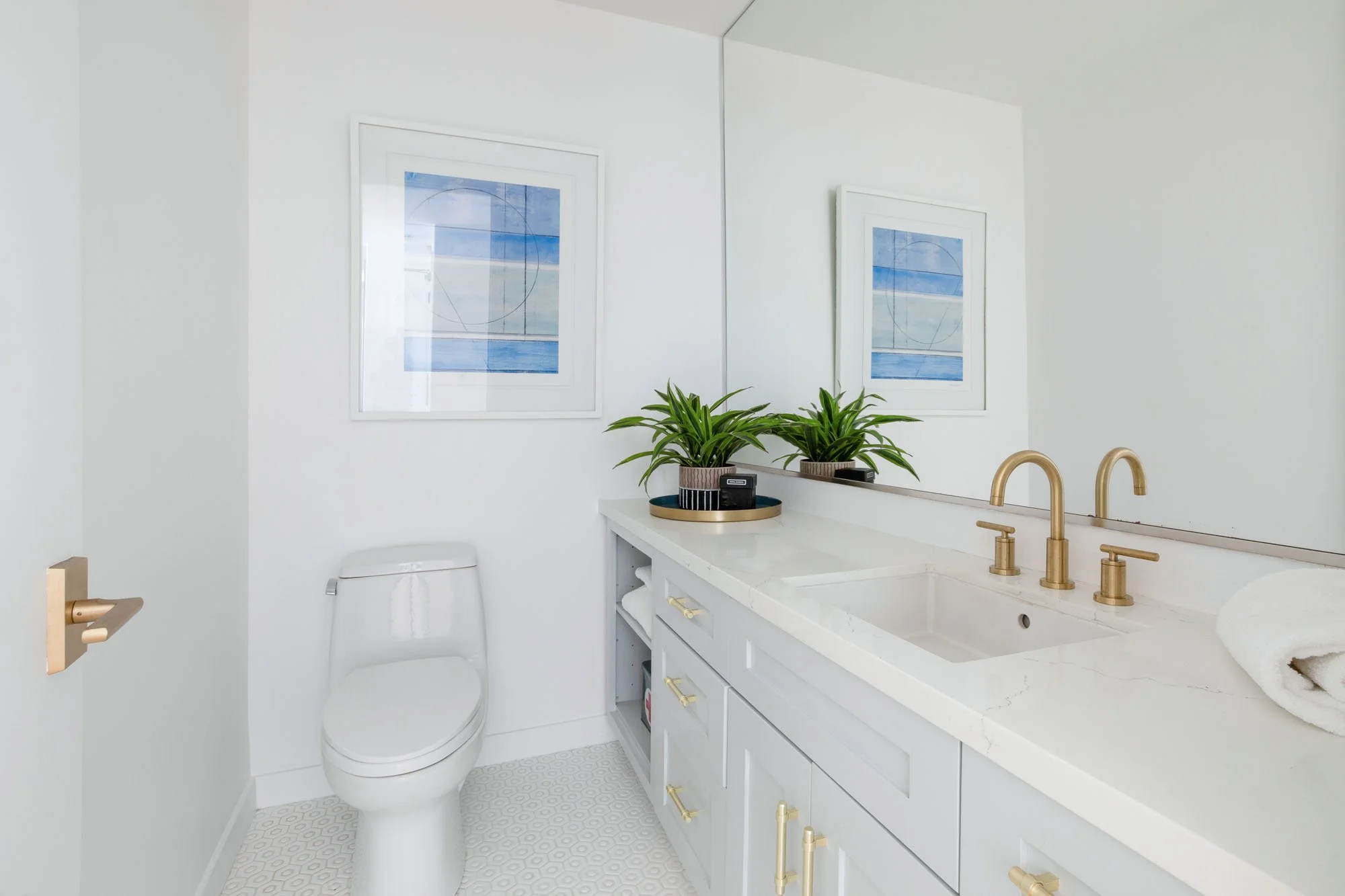 Modern white bathroom design featuring a quartz-top vanity, satin gold faucets and hardware, and white penny tile flooring.