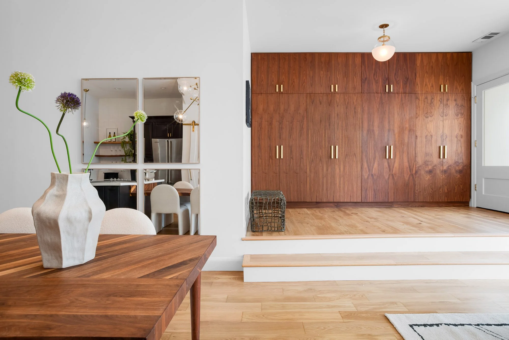 Custom floor-to-ceiling walnut built-in cabinetry with brass hardware on raised platform in San Francisco luxury TIC — media wall with concealed storage, white oak herringbone floors, and sculptural ceramic vase on dining table