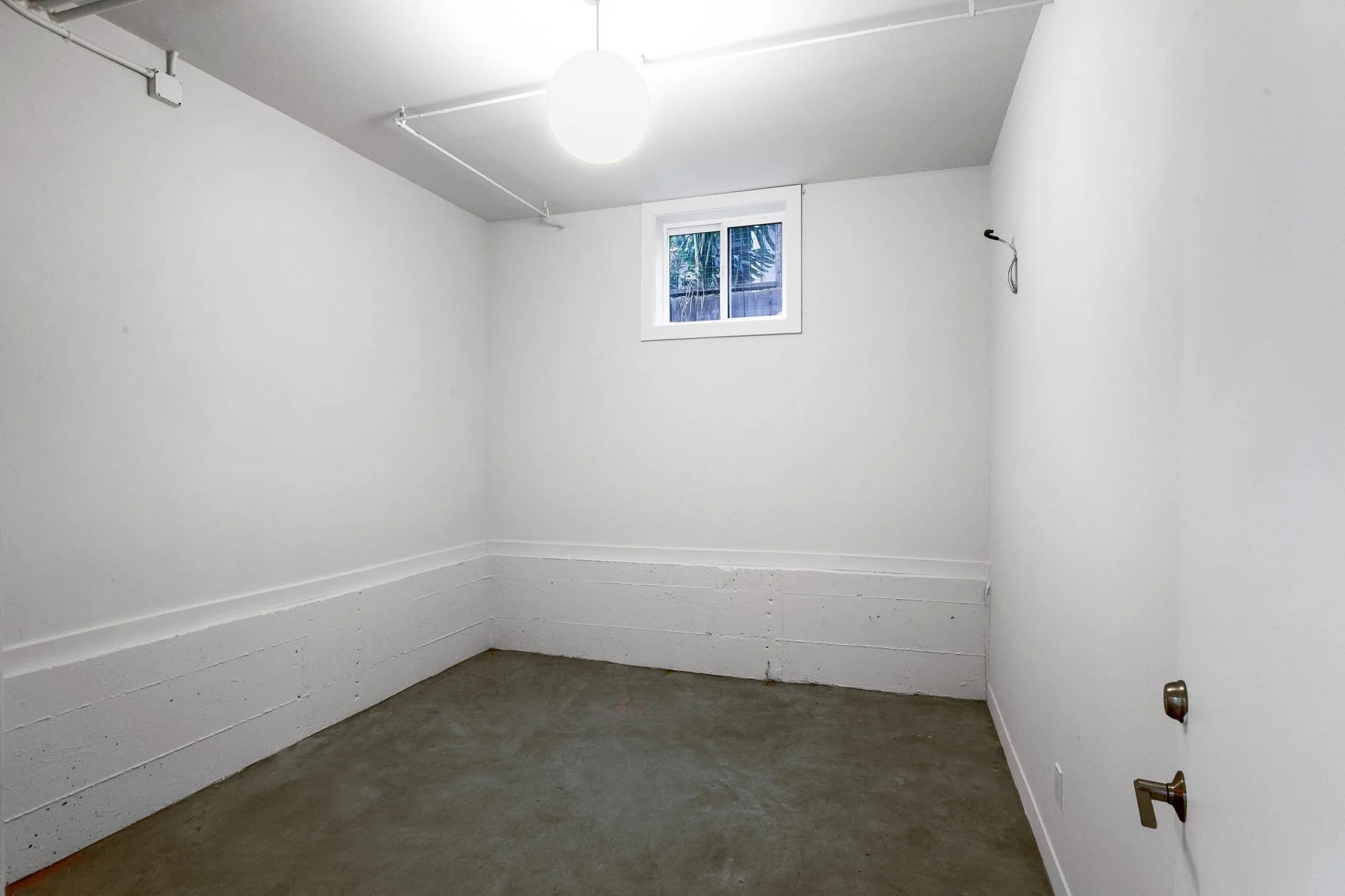 Private secure storage room in a Mission Dolores luxury condo building featuring clean white walls and concrete flooring.