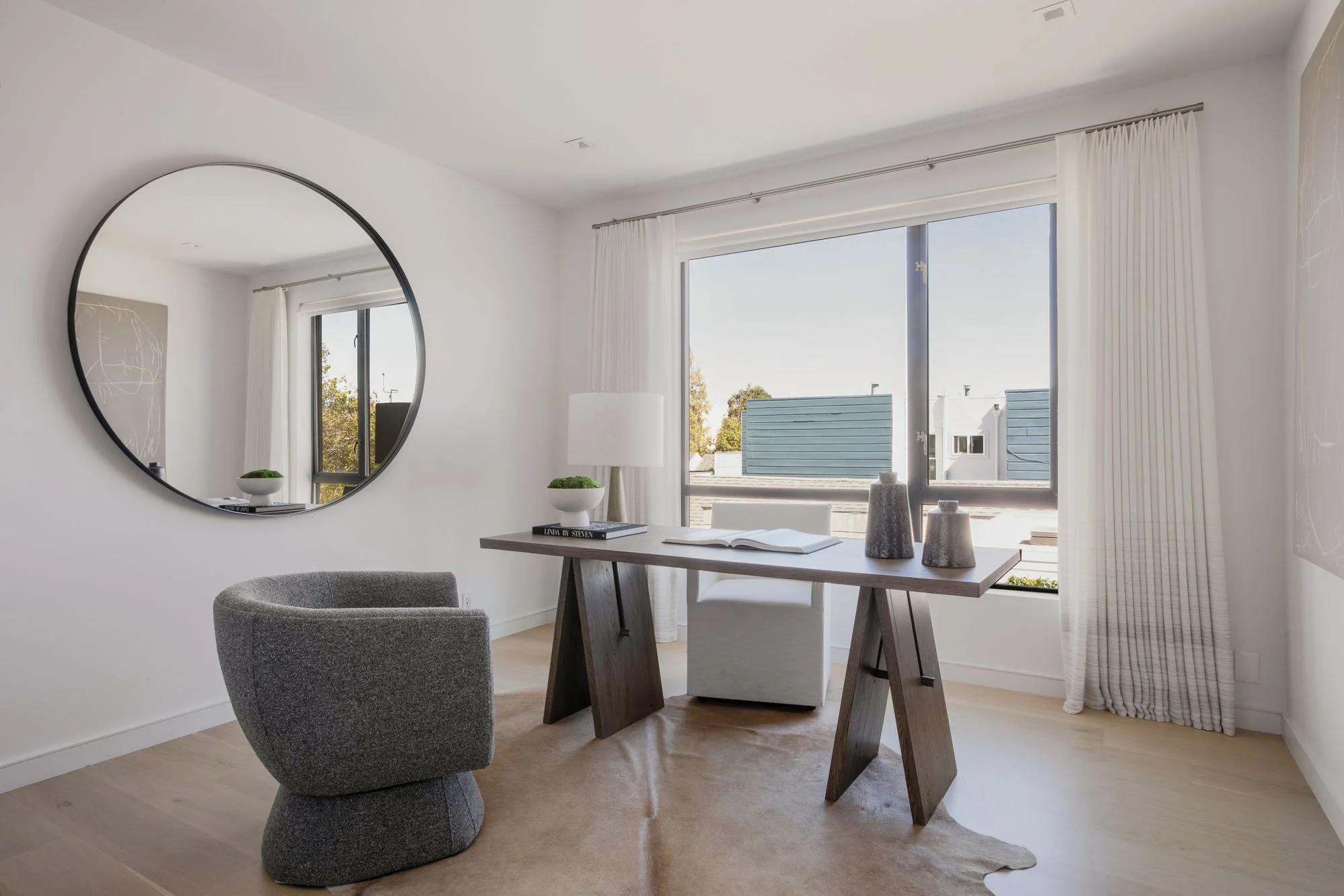 Sophisticated home office at 1647 Sanchez with a minimalist wood trestle desk, large circular mirror, and a gray boucle executive chair.