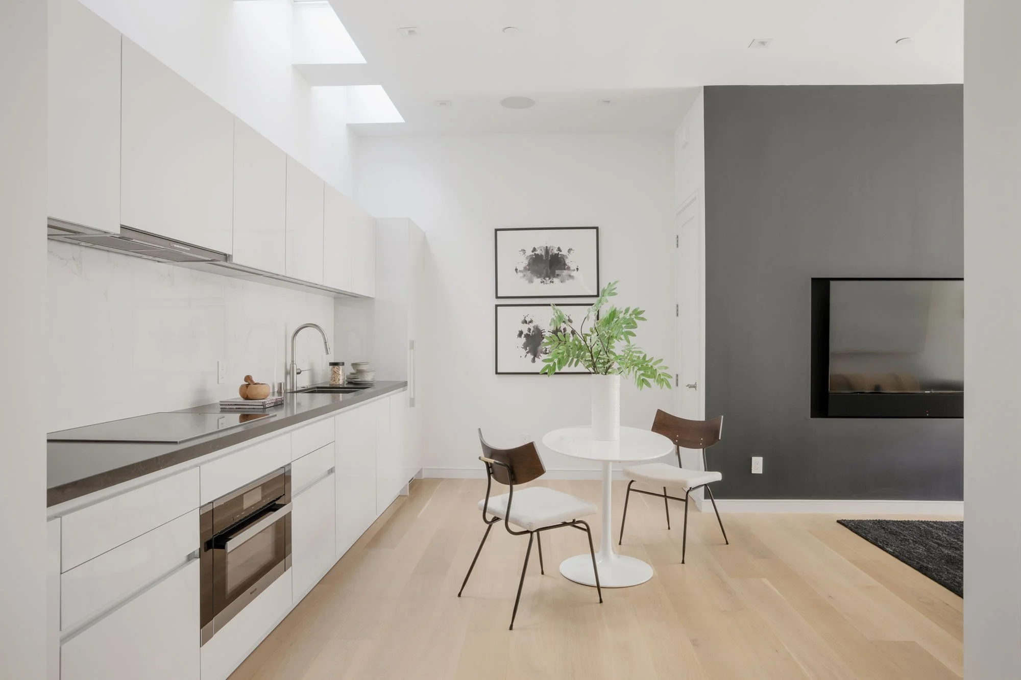 Minimalist designer kitchen and casual dining nook at 290 Day Street, San Francisco, featuring integrated white cabinetry, skylights, and a custom charcoal accent wall.