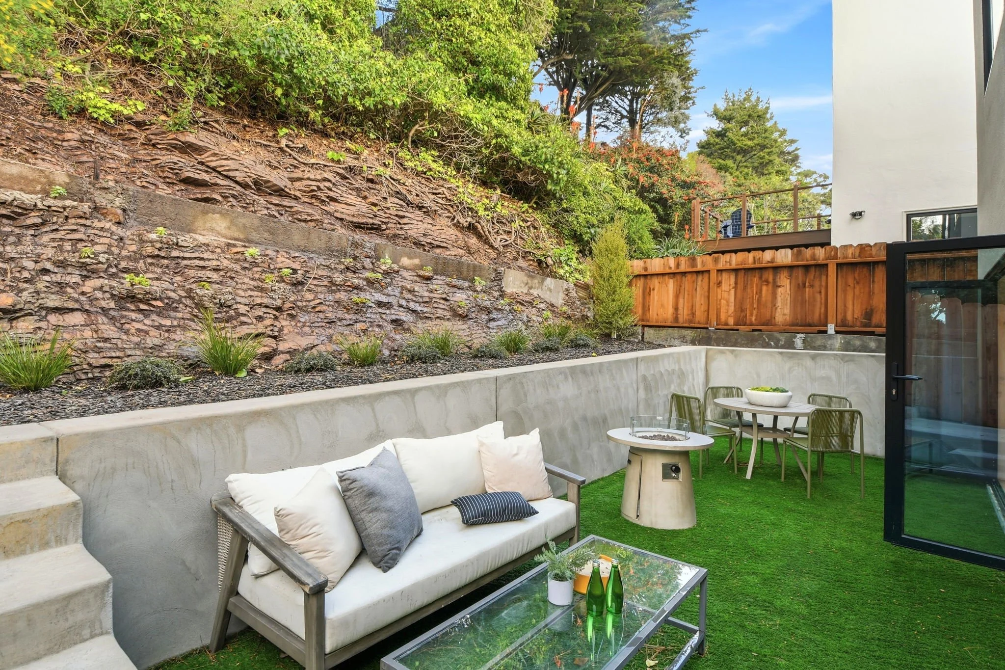 Private backyard oasis in Midtown Terrace, San Francisco, featuring a modern outdoor sofa, glass coffee table, fire pit, and professional artificial turf landscaping.