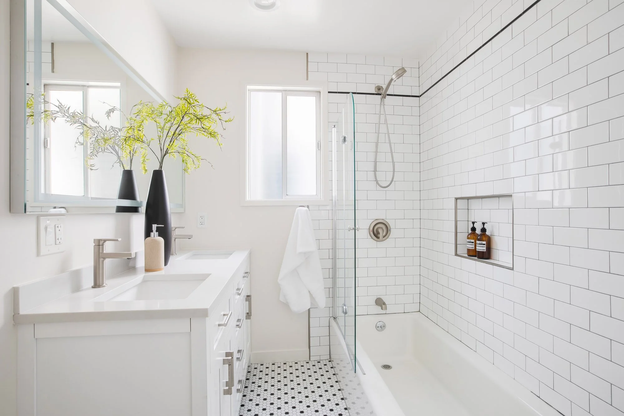 Bathroom at 465 30th Street with a double vanity, white subway tile tub and shower with glass panel and built-in niche, and black-and-white hexagonal mosaic tile floor