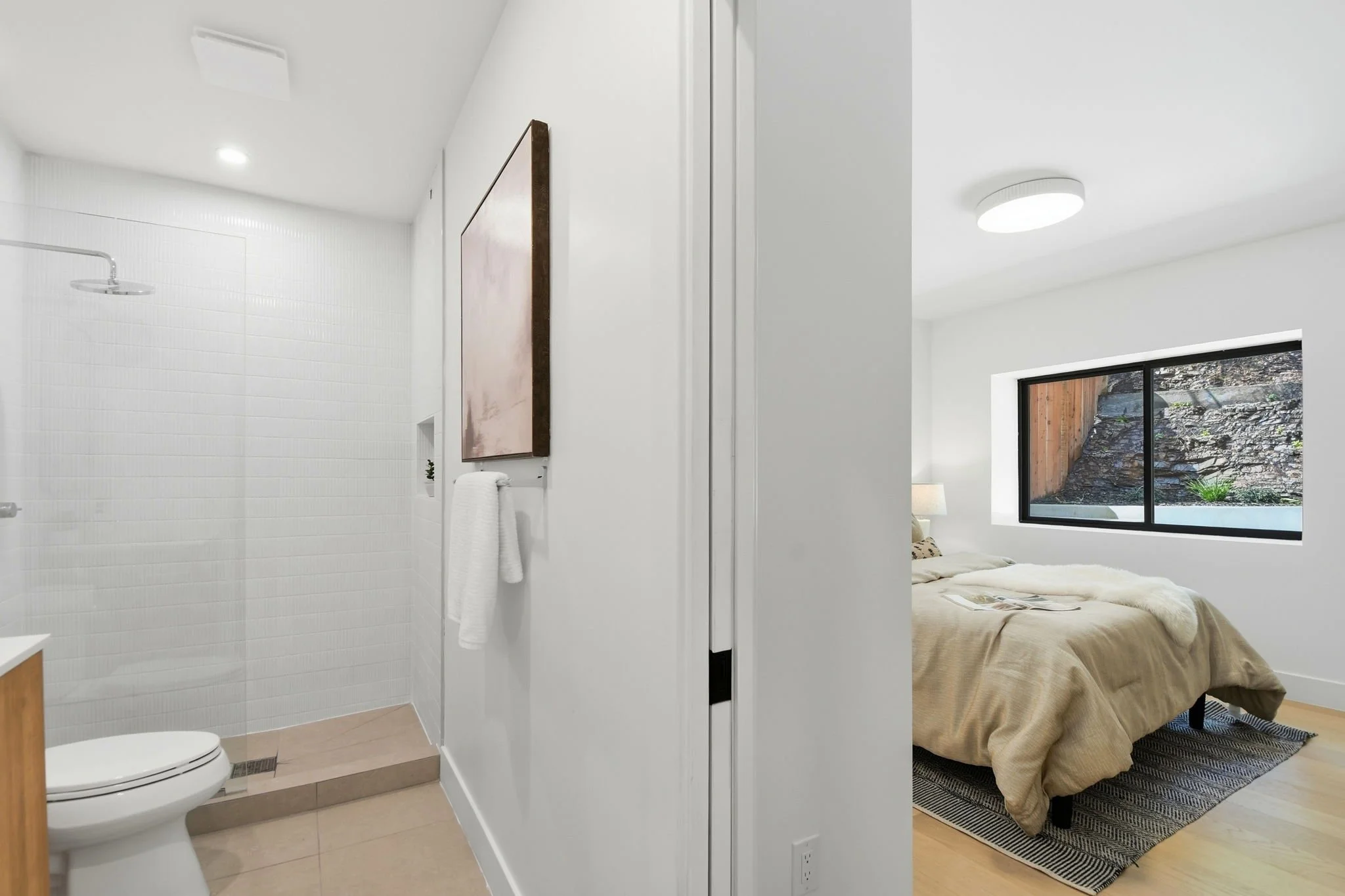 Modern bathroom renovation featuring a walk-in rain shower with minimalist white tile and a transition into a sun-drenched bedroom.