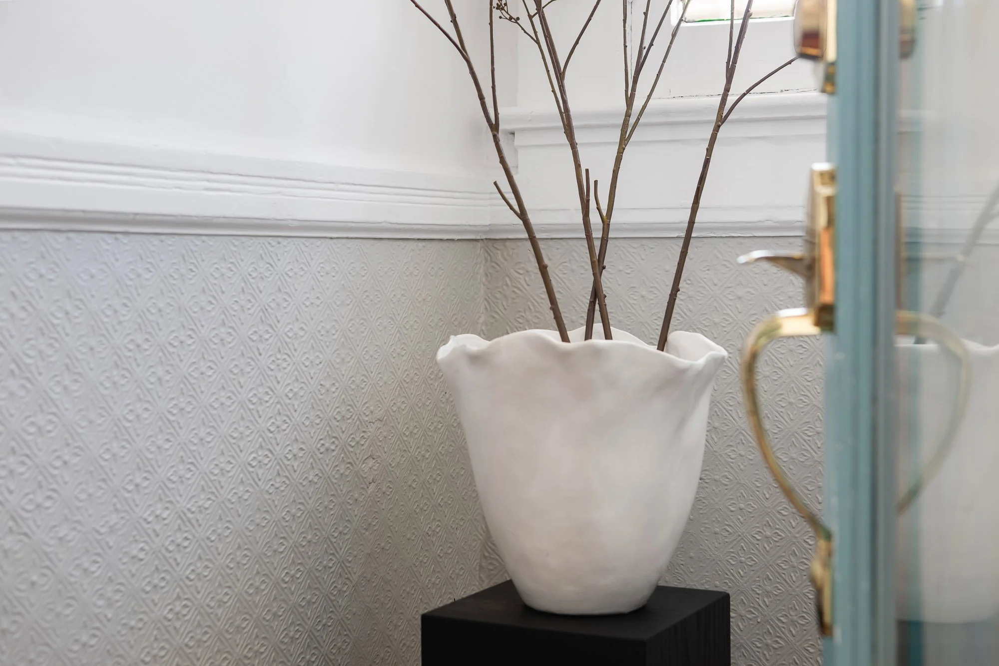 Decorative vase on a pedestal against textured wainscotting near a glass-paned door