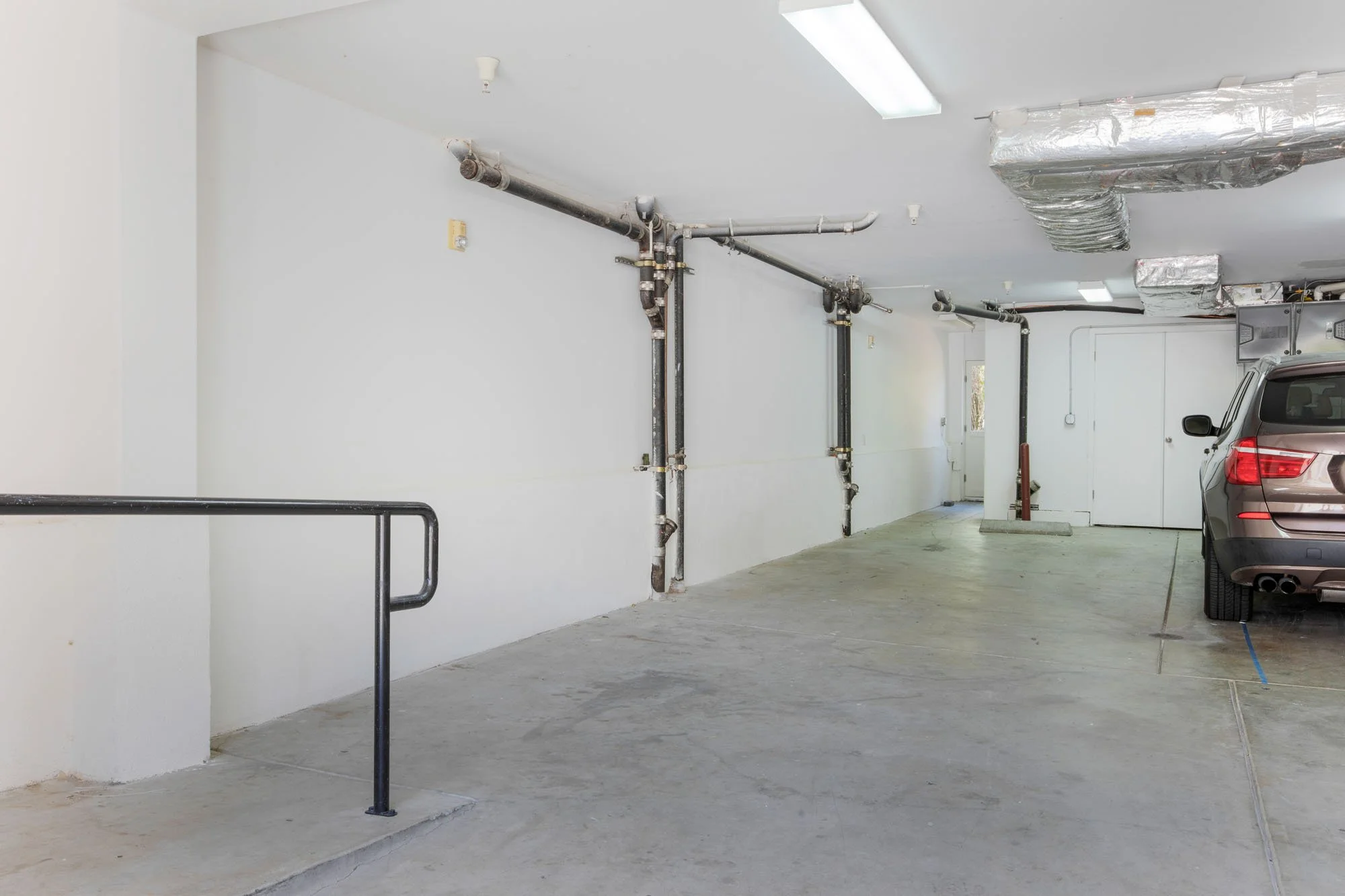 Interior view of a clean, spacious attached garage with concrete flooring, exposed utility piping, and modern HVAC ductwork.