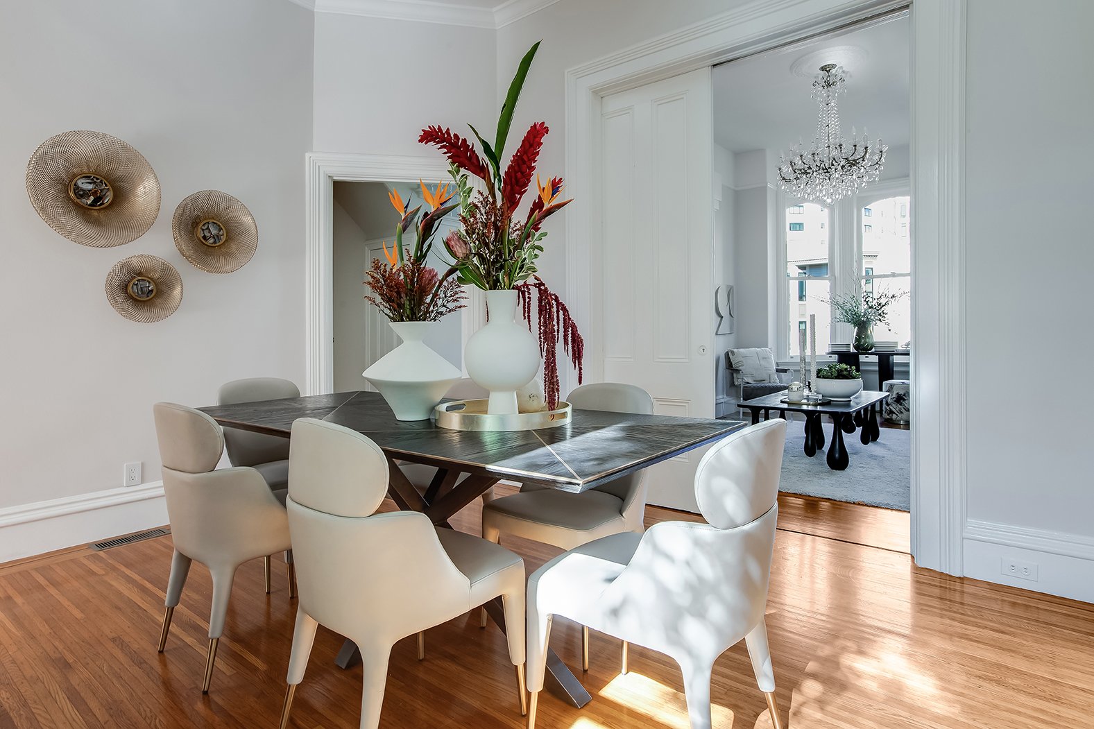 Luxury dining room with white pocket doors leading to a grand living room with a crystal chandelier and classic architectural moldings.