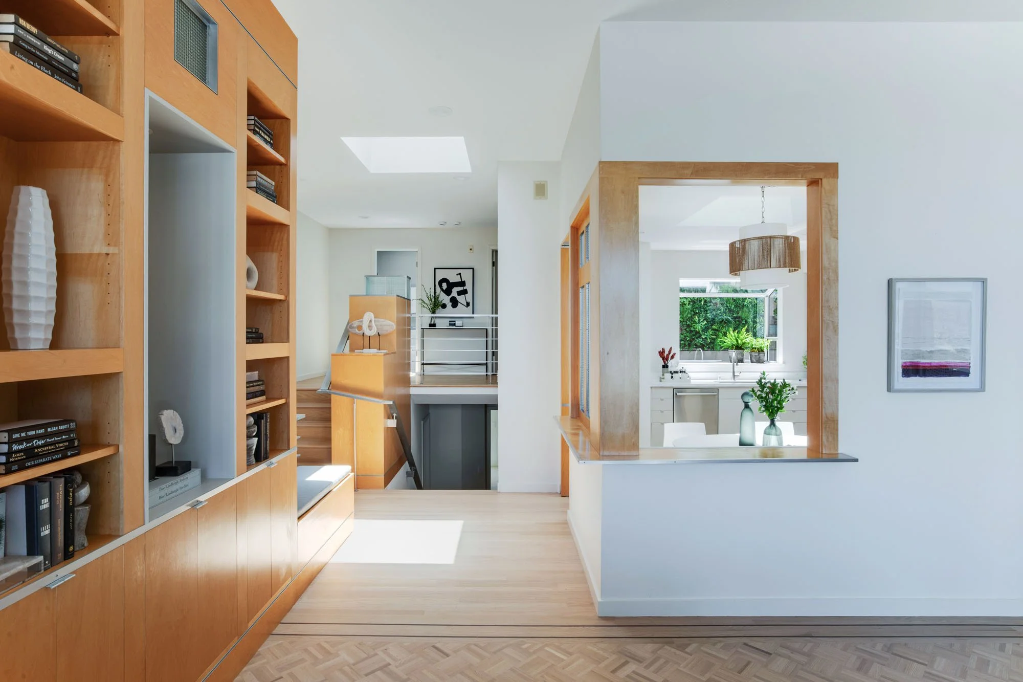 Contemporary home interior highlighting the open-concept layout with views from the living area through a wood-framed portal into a bright, modern designer kitchen.