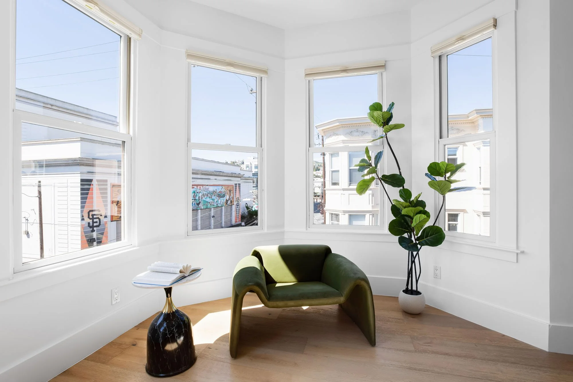 Sunny bay window reading nook in a San Francisco home featuring a green velvet lounge chair and views of the Mission District.