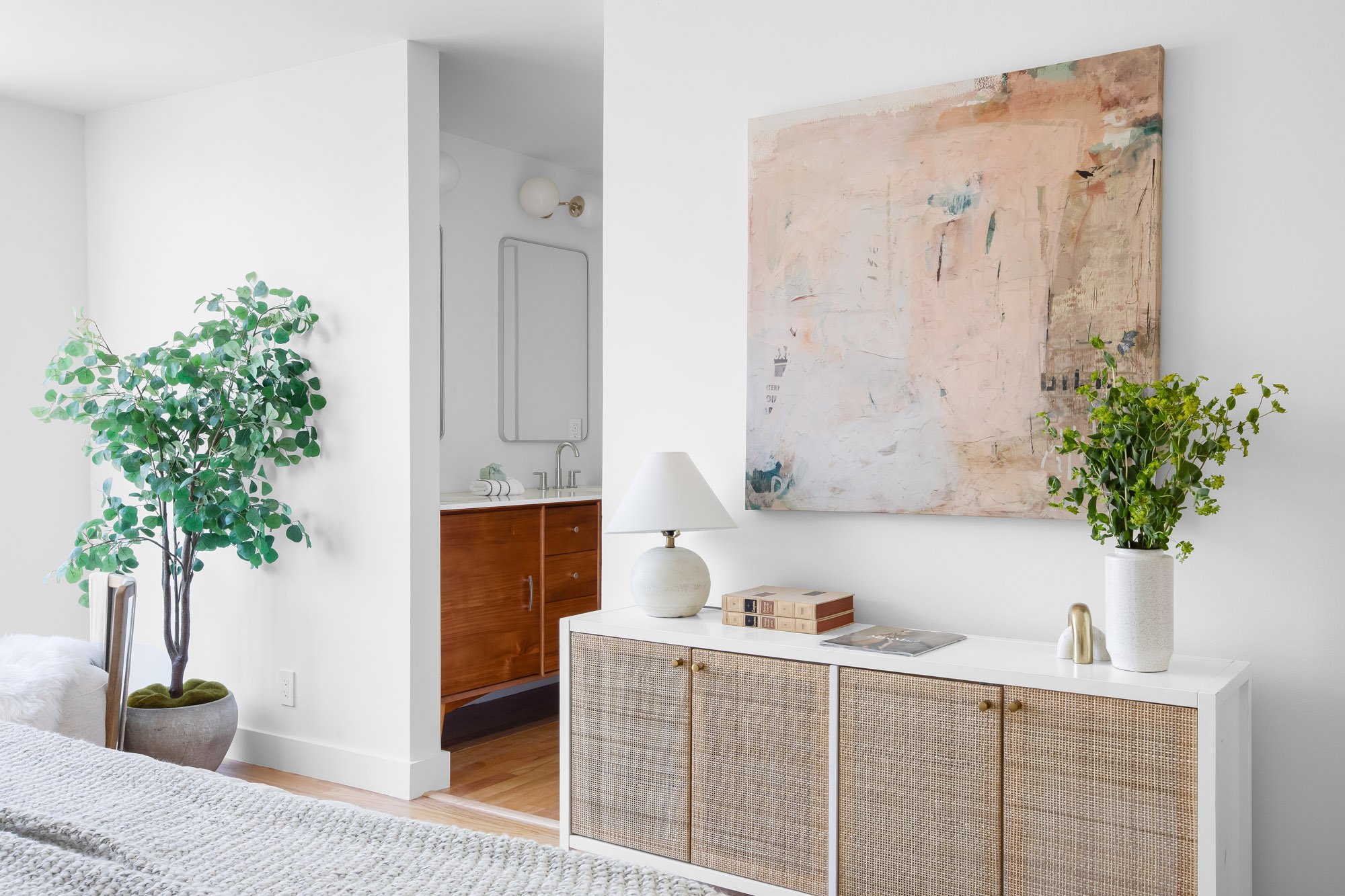 Primary suite at 932 Broderick Street #2 showing the en-suite bathroom with mid-century wood vanity and a rattan dresser with abstract artwork.