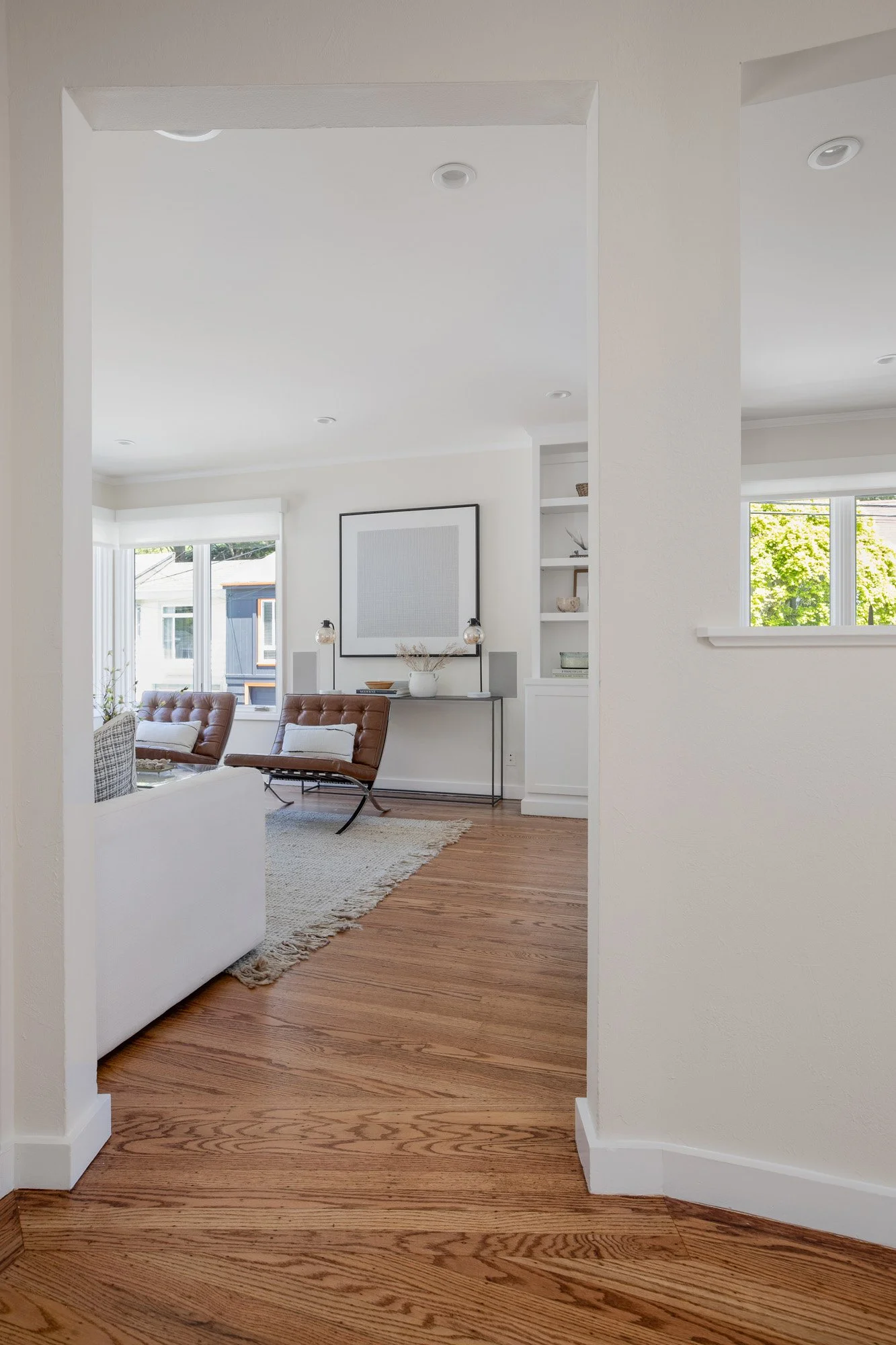 View from the entryway into a modern living room featuring leather Barcelona-style chairs and large picture windows.