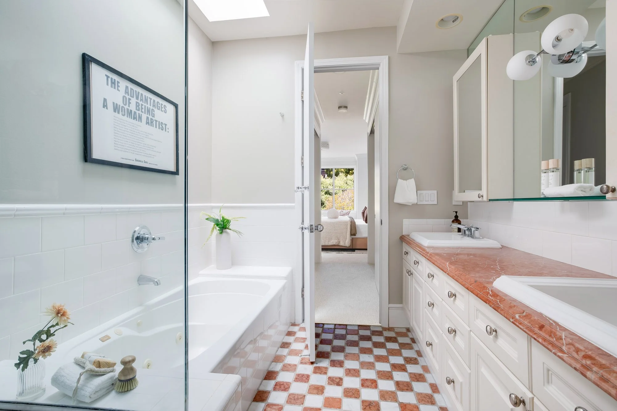 Primary bathroom at 2172 Fell Street San Francisco showing soaking tub, glass shower partition, double vanity with rose marble countertop, skylight, chrome fixtures, and open door to carpeted primary bedroom