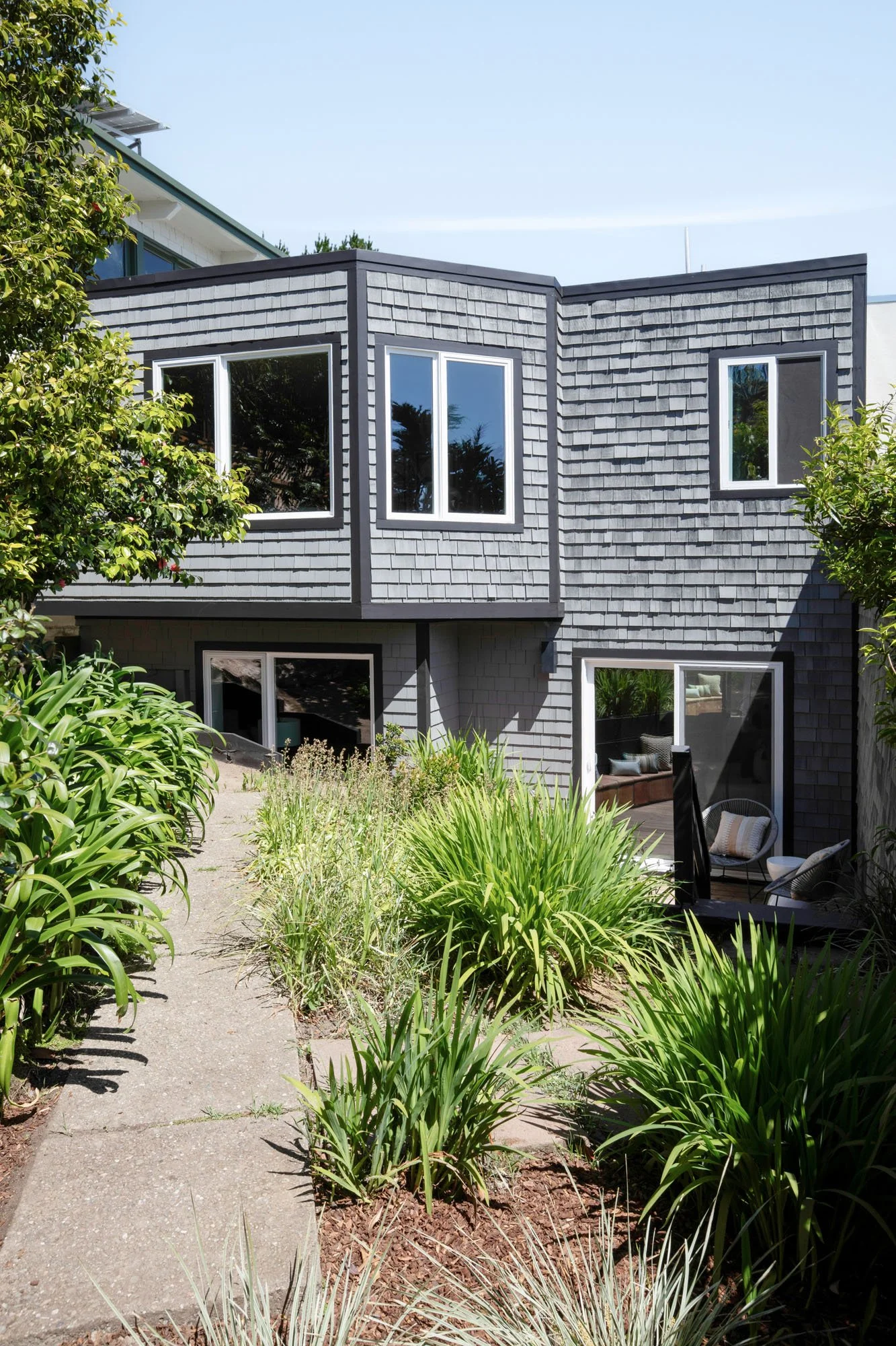 Vertical architectural view of a modern San Francisco home with grey shingle siding and lush garden landscaping leading to a private lower-level entrance.