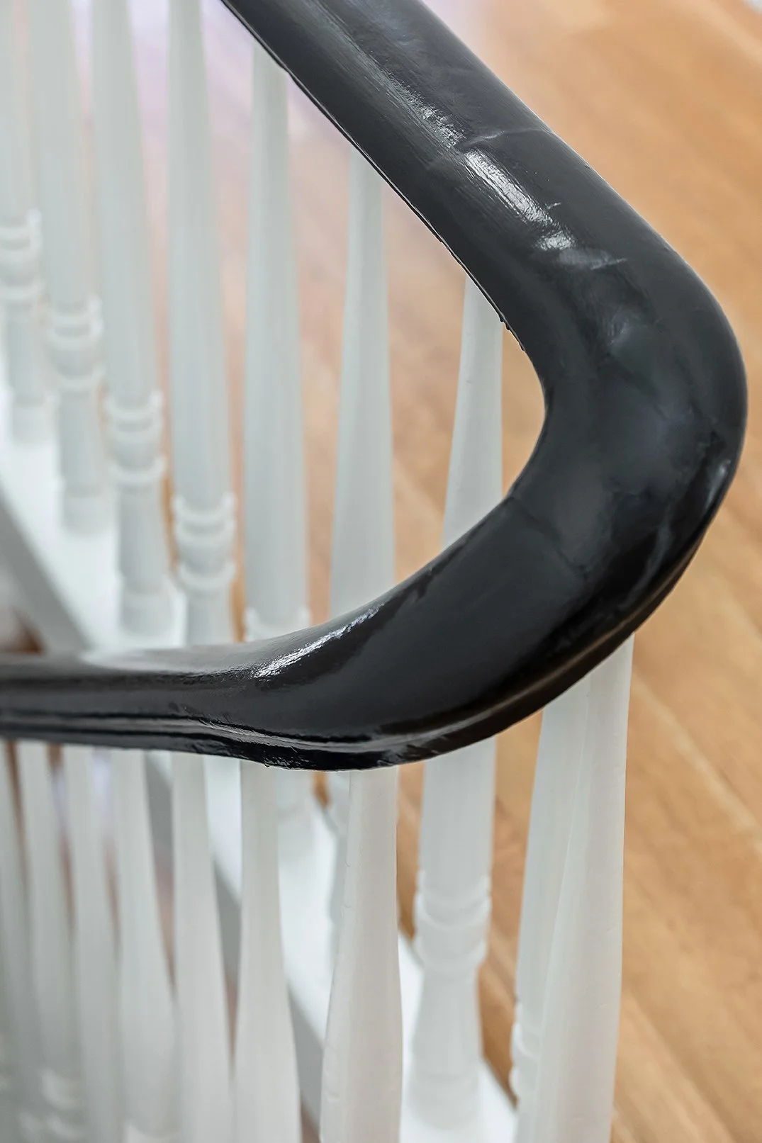 Close-up of a traditional Victorian staircase featuring a high-gloss black handrail and elegant white spindles in a renovated San Francisco luxury home.
