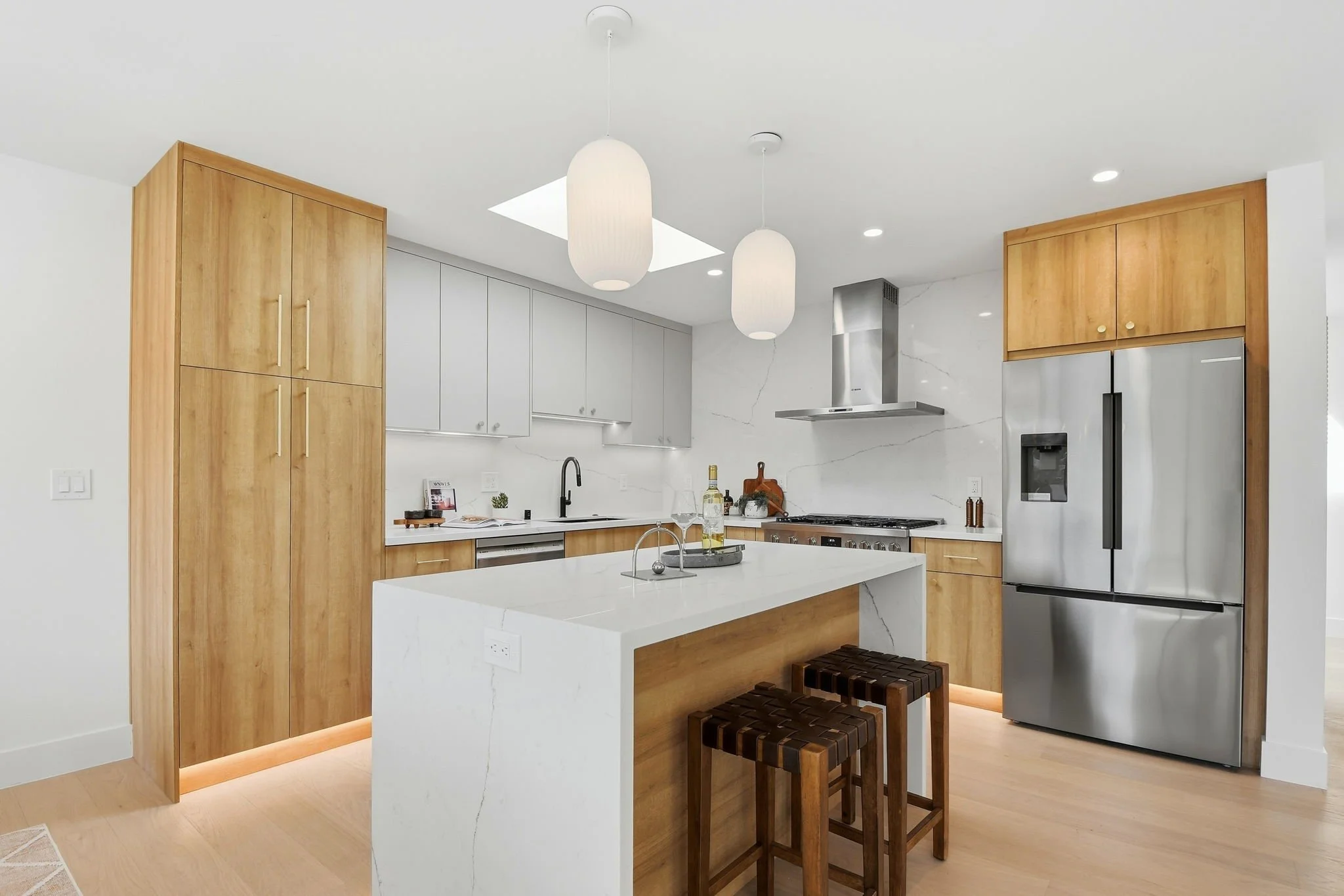 Contemporary chef's kitchen with a marble waterfall island, stainless steel appliances, and custom light-wood cabinetry in a luxury San Francisco home.