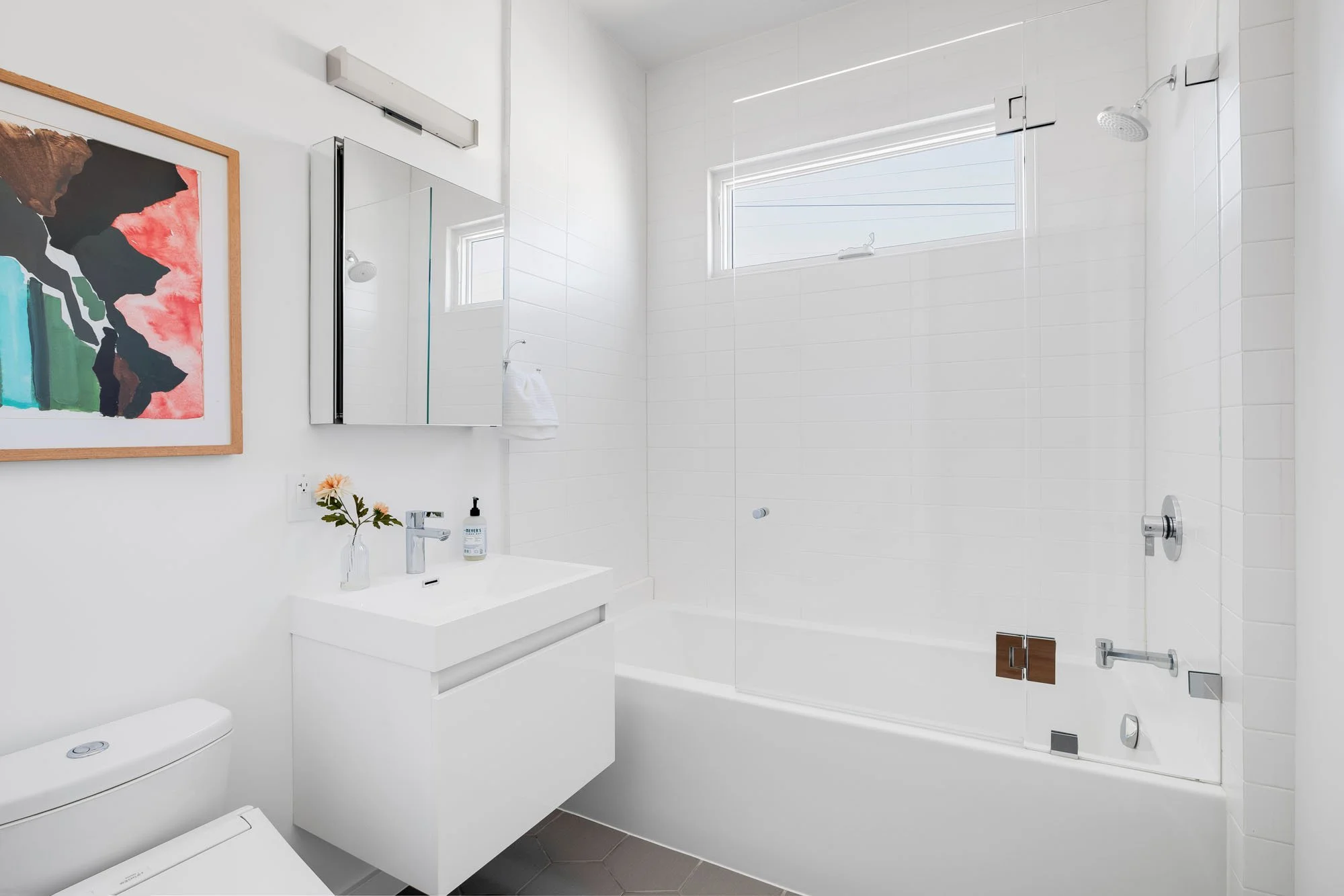 Contemporary bathroom with a white floating vanity, modern subway tile, and a glass-enclosed bathtub in a renovated SF apartment.