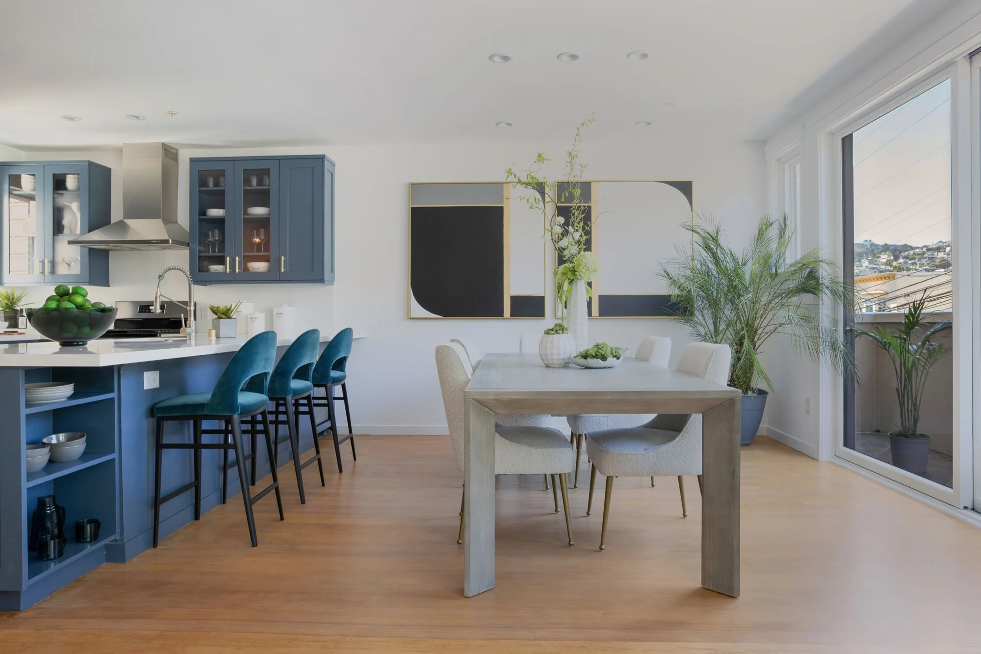 Modern open-concept kitchen and dining area featuring slate blue shaker cabinets, white quartz countertops, and a light wood dining table with upholstered chairs.