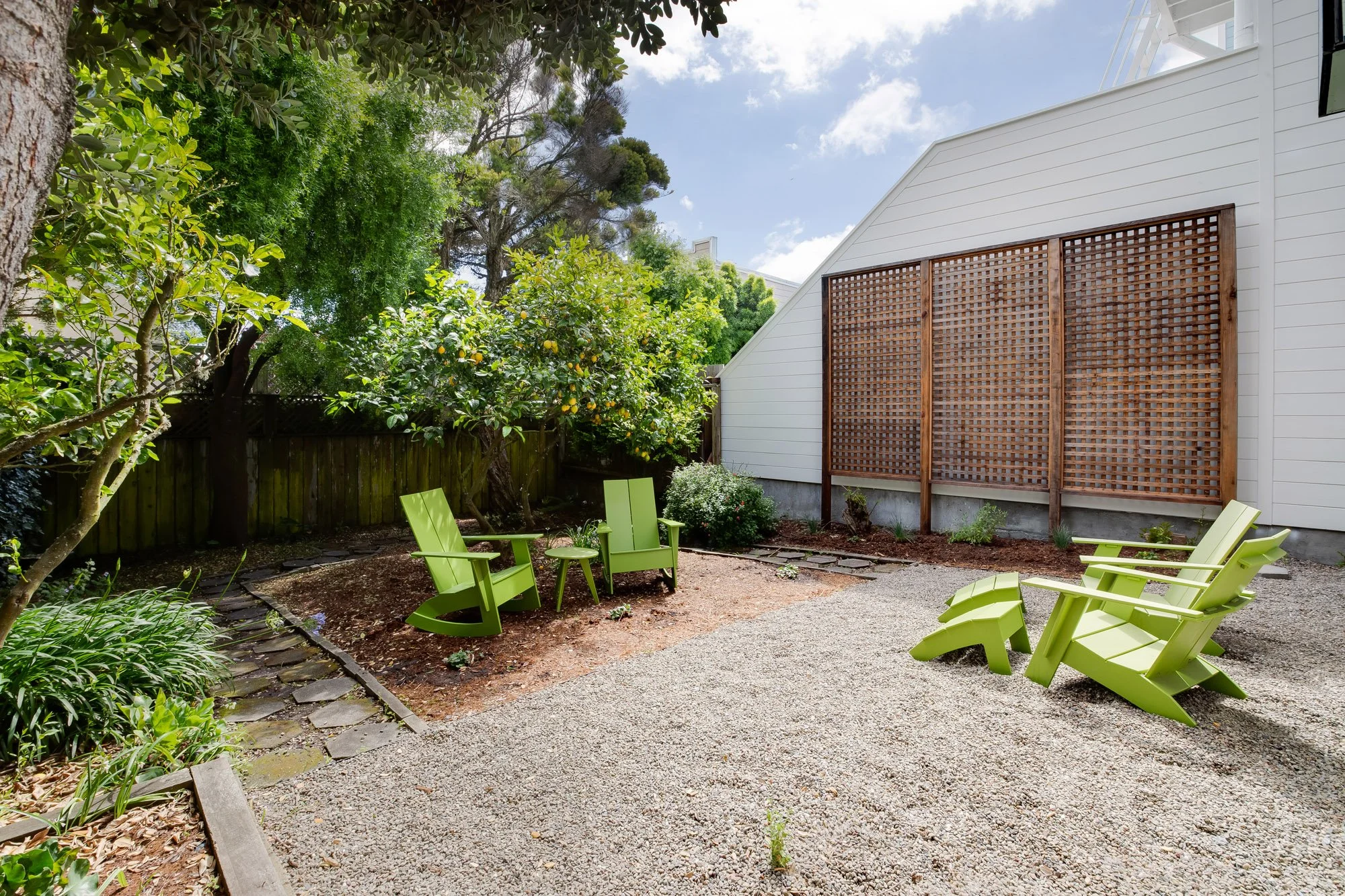 Shared rear garden with mature lemon tree, gravel patio, flagstone path, wooden privacy trellis, and Adirondack seating in luxury Presidio Heights Victorian flat, San Francisco