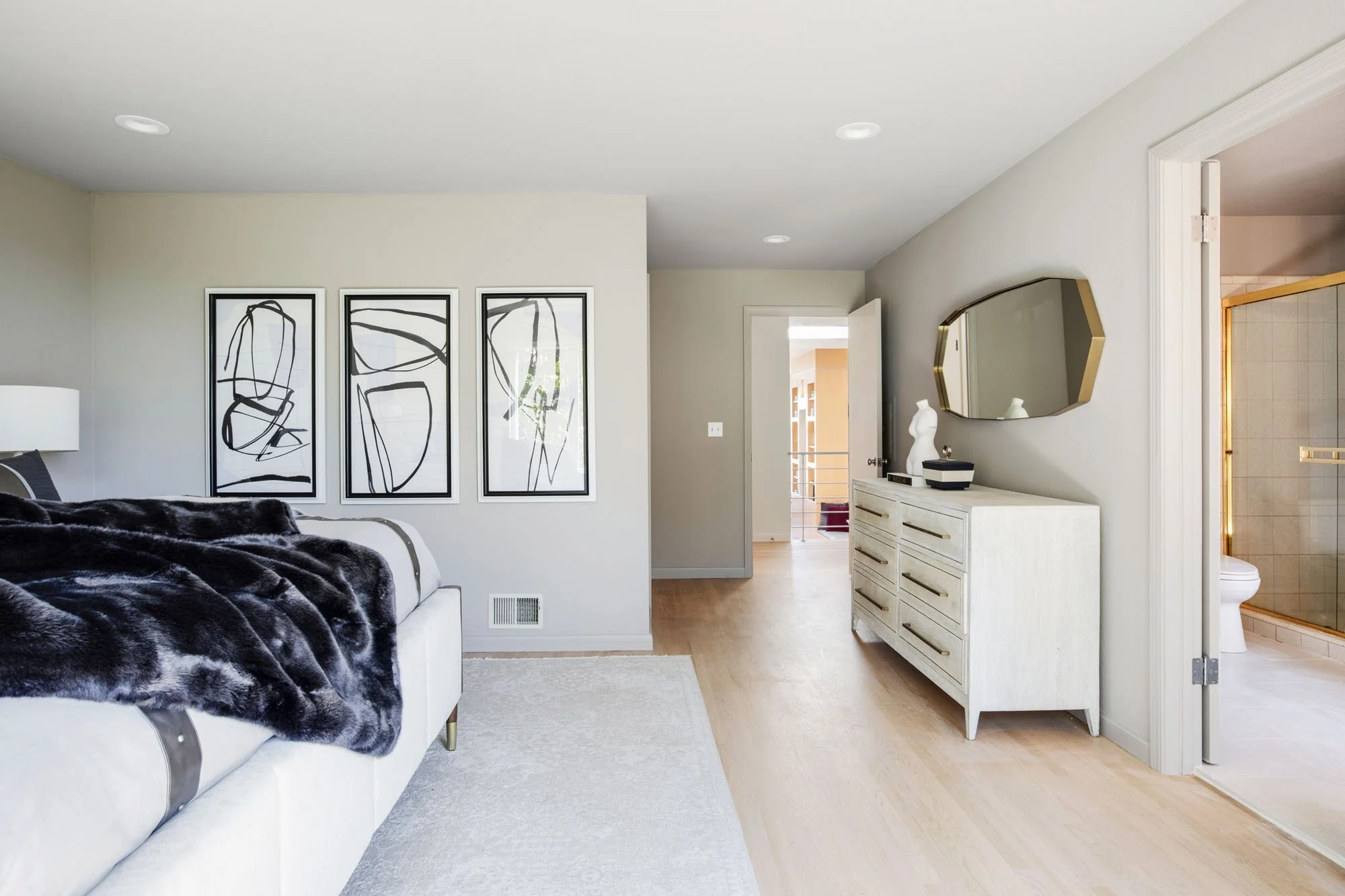 Contemporary primary bedroom layout showing three abstract black-and-white art prints, a sleek white dresser, and an entrance to the ensuite bathroom.
