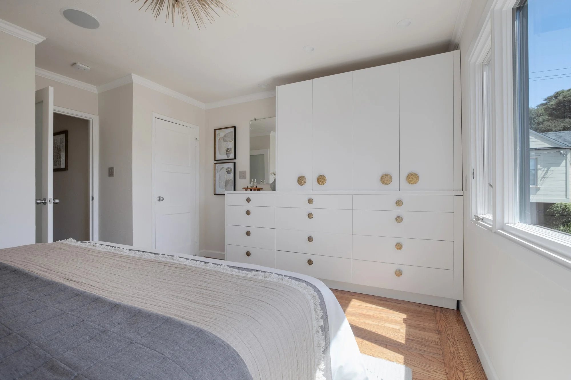 Spacious bedroom with custom white built-in wardrobes, gold hardware, and large windows overlooking the neighborhood.