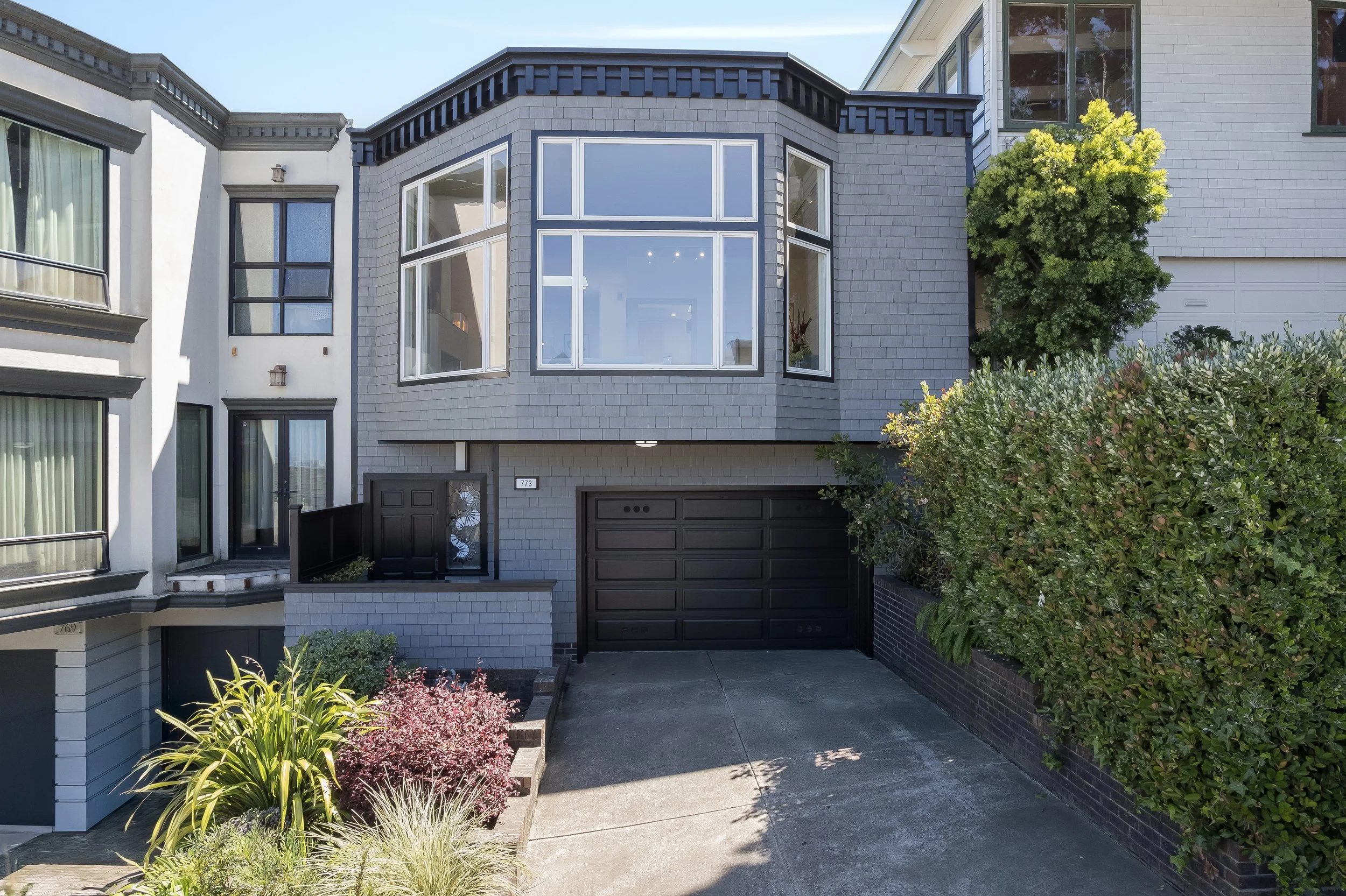 Modern San Francisco home exterior at 773 Duncan Street featuring grey shingle siding, a sleek black two-car garage door, and a unique piano-key stained glass sidelight.