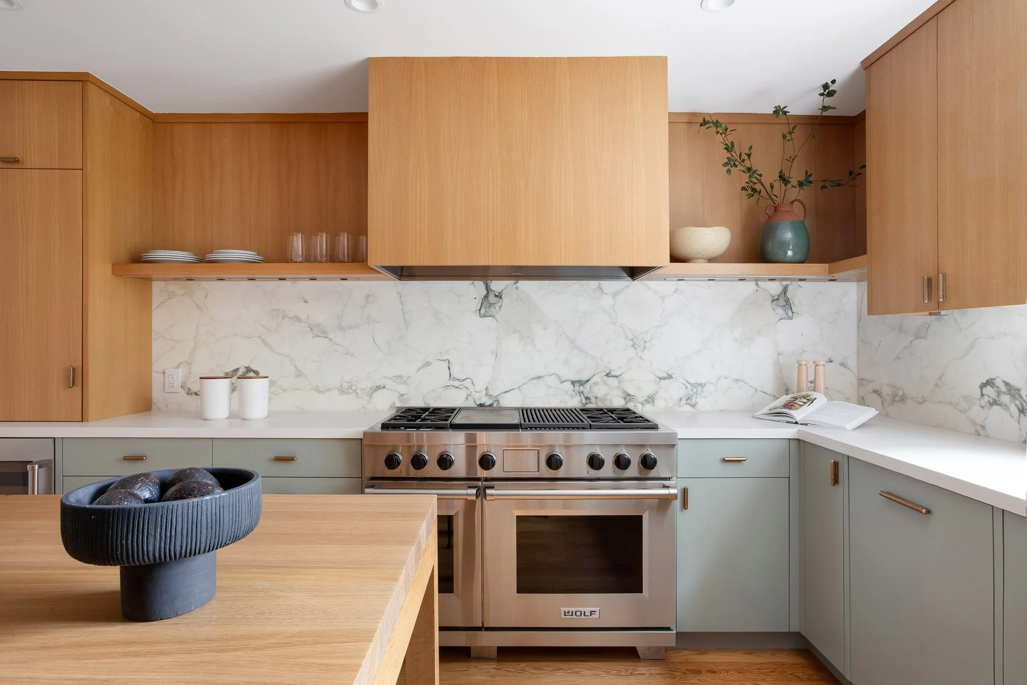 Renovated chef's kitchen at 771 Elizabeth Street with a stainless Wolf 48-inch dual-fuel range, full-height marble backsplash, white oak and sage green cabinetry, and a custom oak island. 