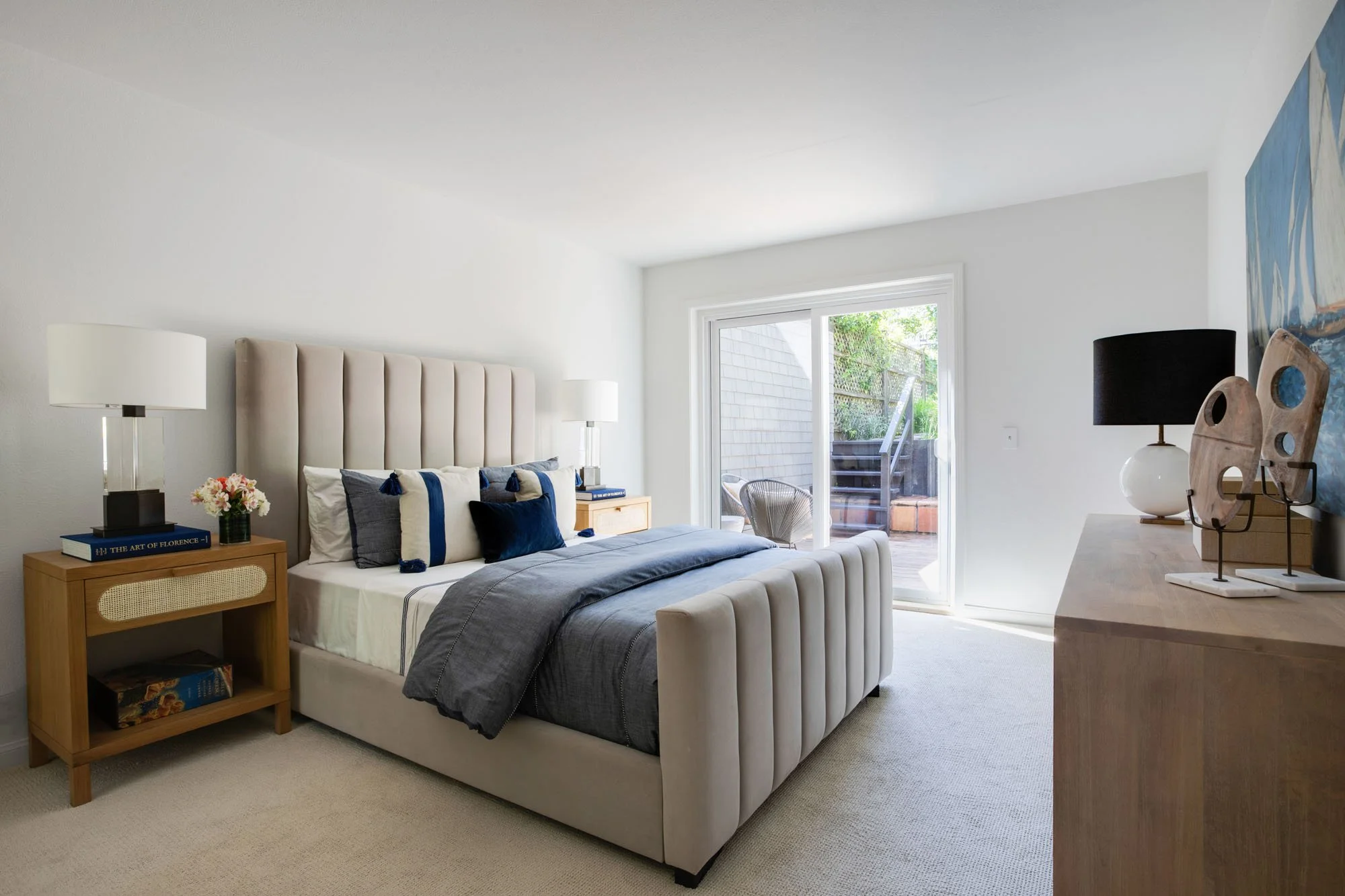An alternate view of a neutral-toned bedroom with a large sliding door, showcasing an indoor-outdoor living flow and high-end staging with a wood and cane nightstand.