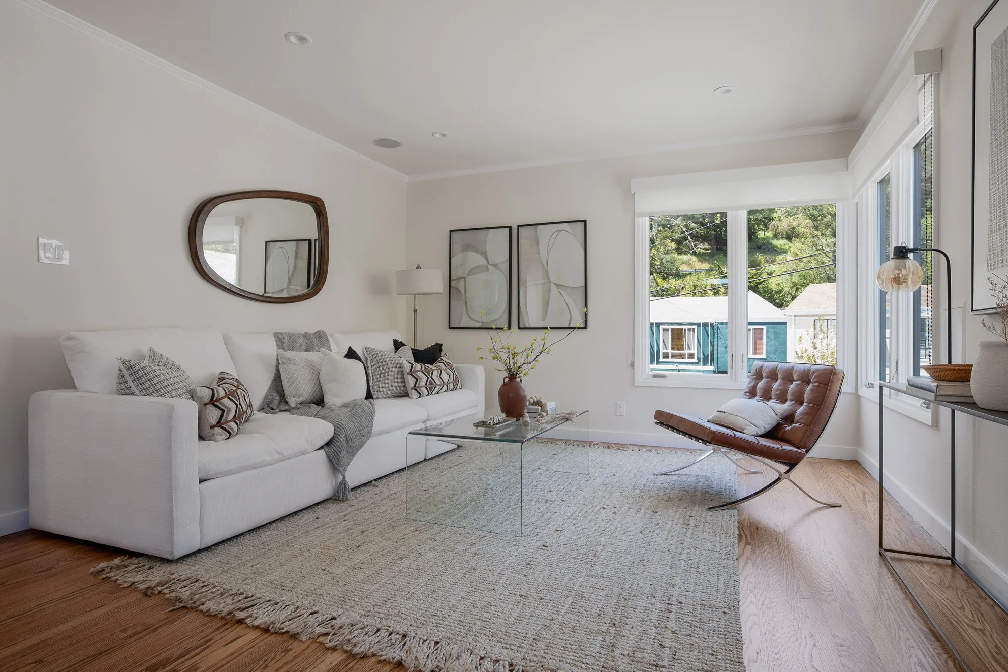 Bright living area with an organic-shaped wood mirror, neutral decor, and large windows overlooking the Glenview neighborhood.