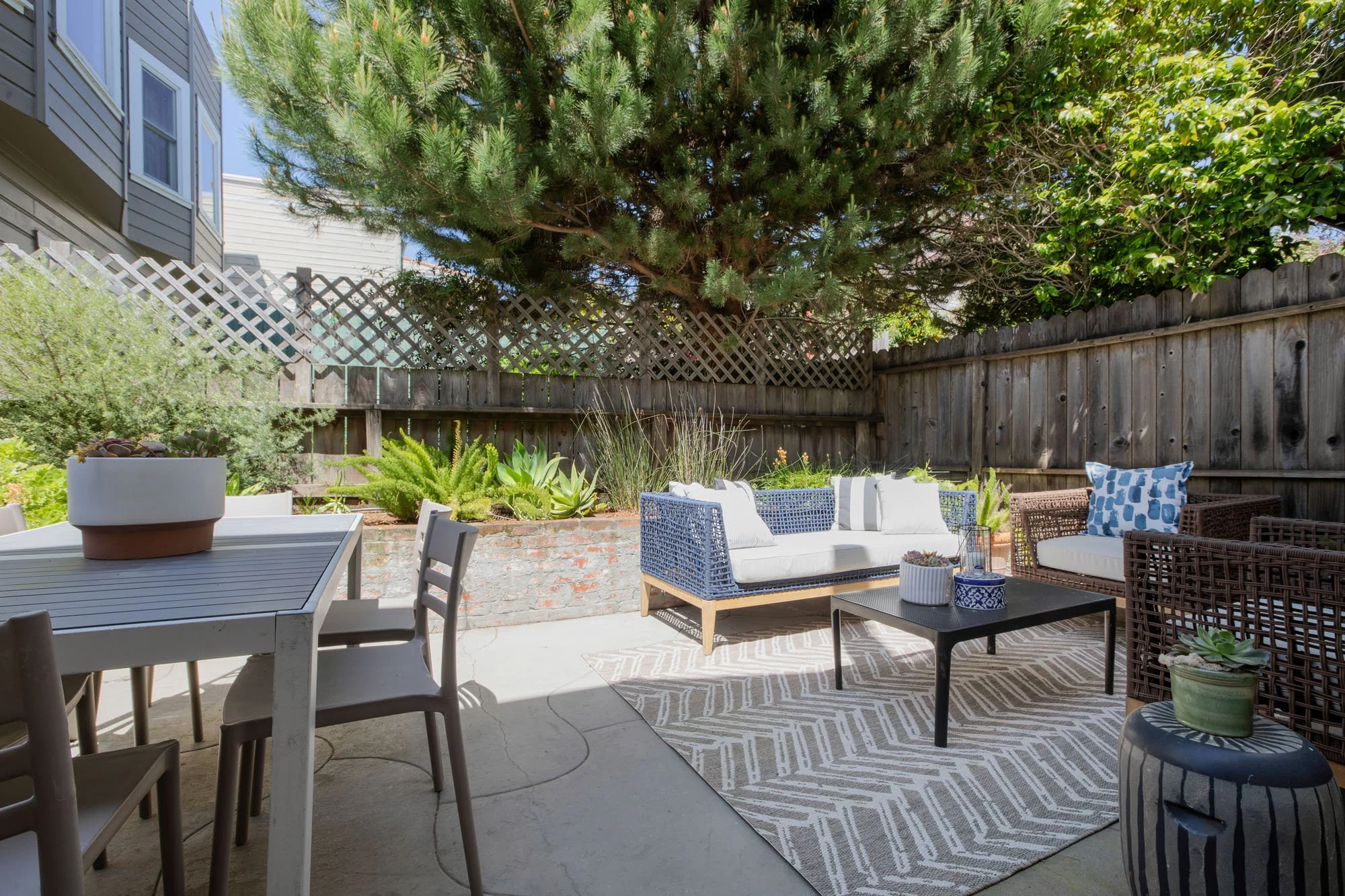 Private urban backyard at 2872 25th St featuring a paved patio, outdoor lounge furniture, a dining area, and mature trees for privacy.